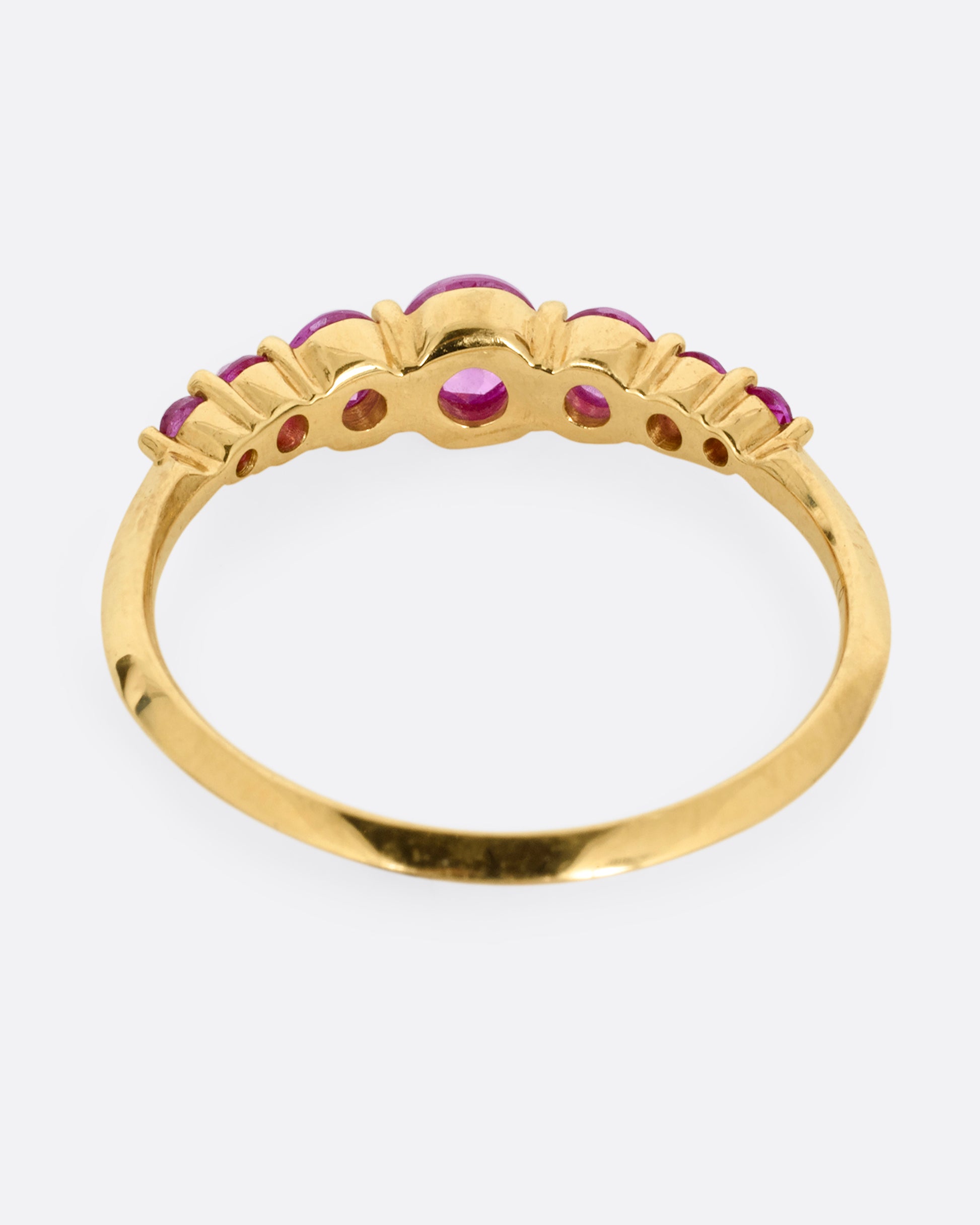 A yellow gold ring with 7 reverse set rubies, shown from the back.