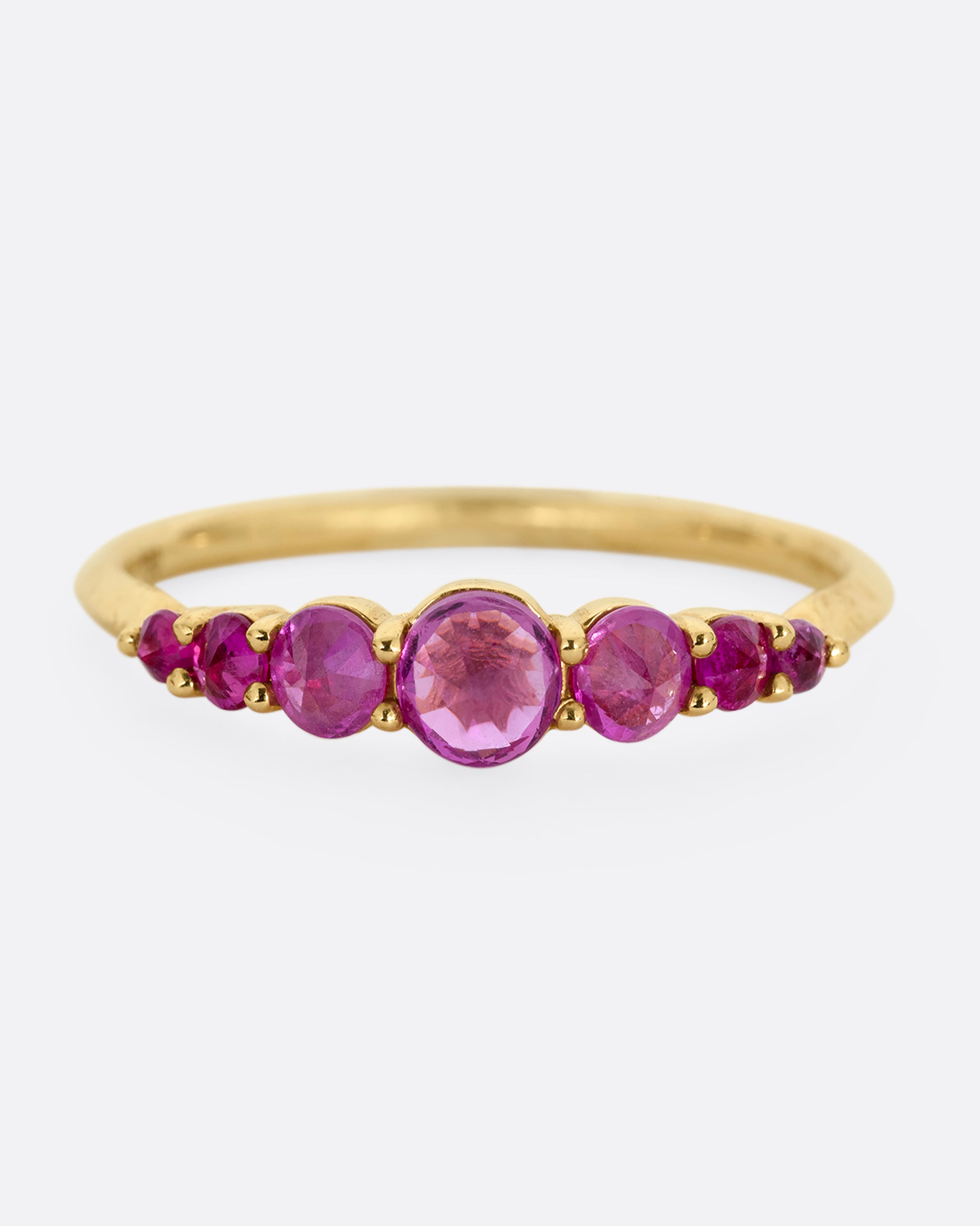 A yellow gold ring with 7 reverse set rubies, shown from the front.