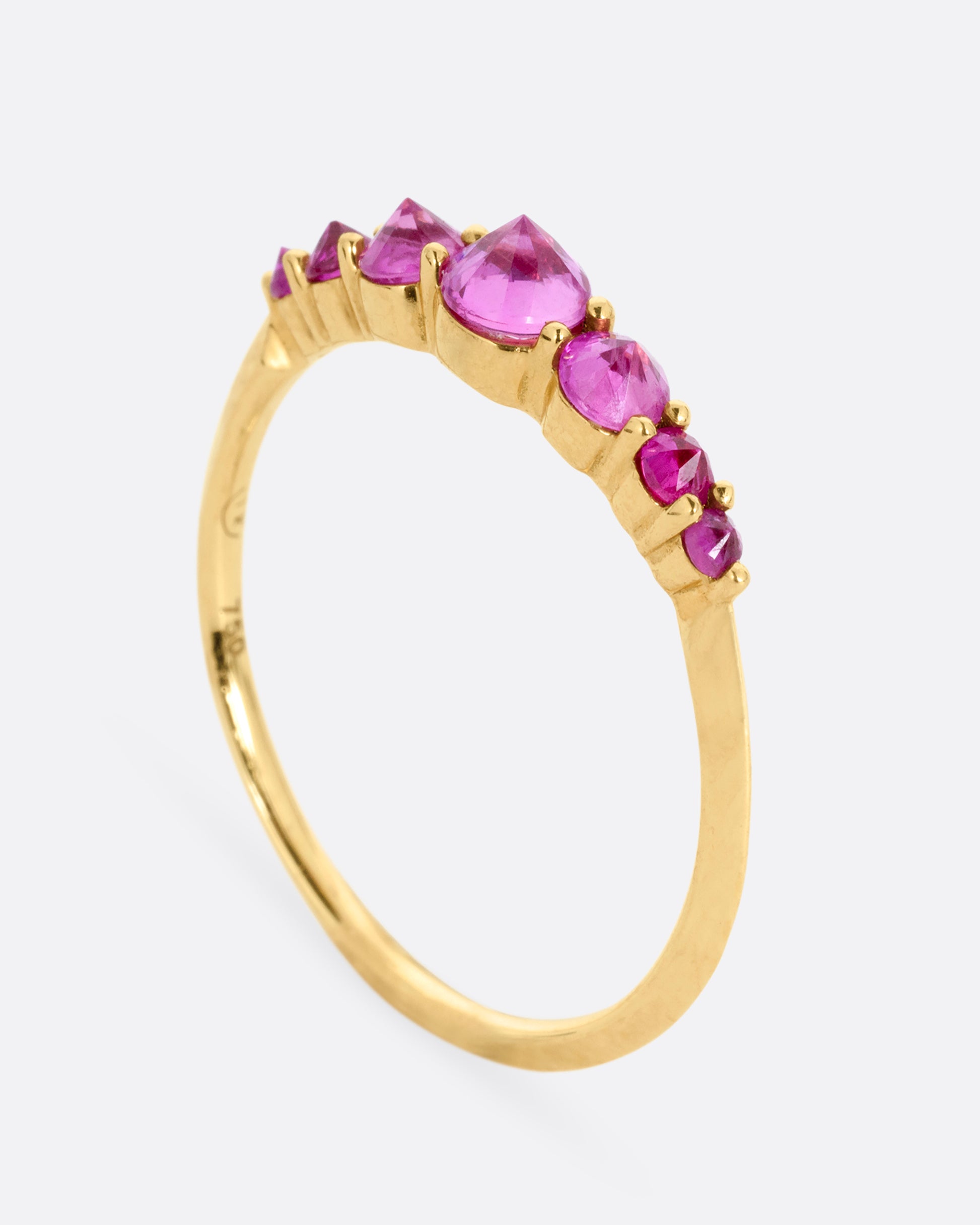 A yellow gold ring with 7 reverse set rubies, shown standing up from the side.