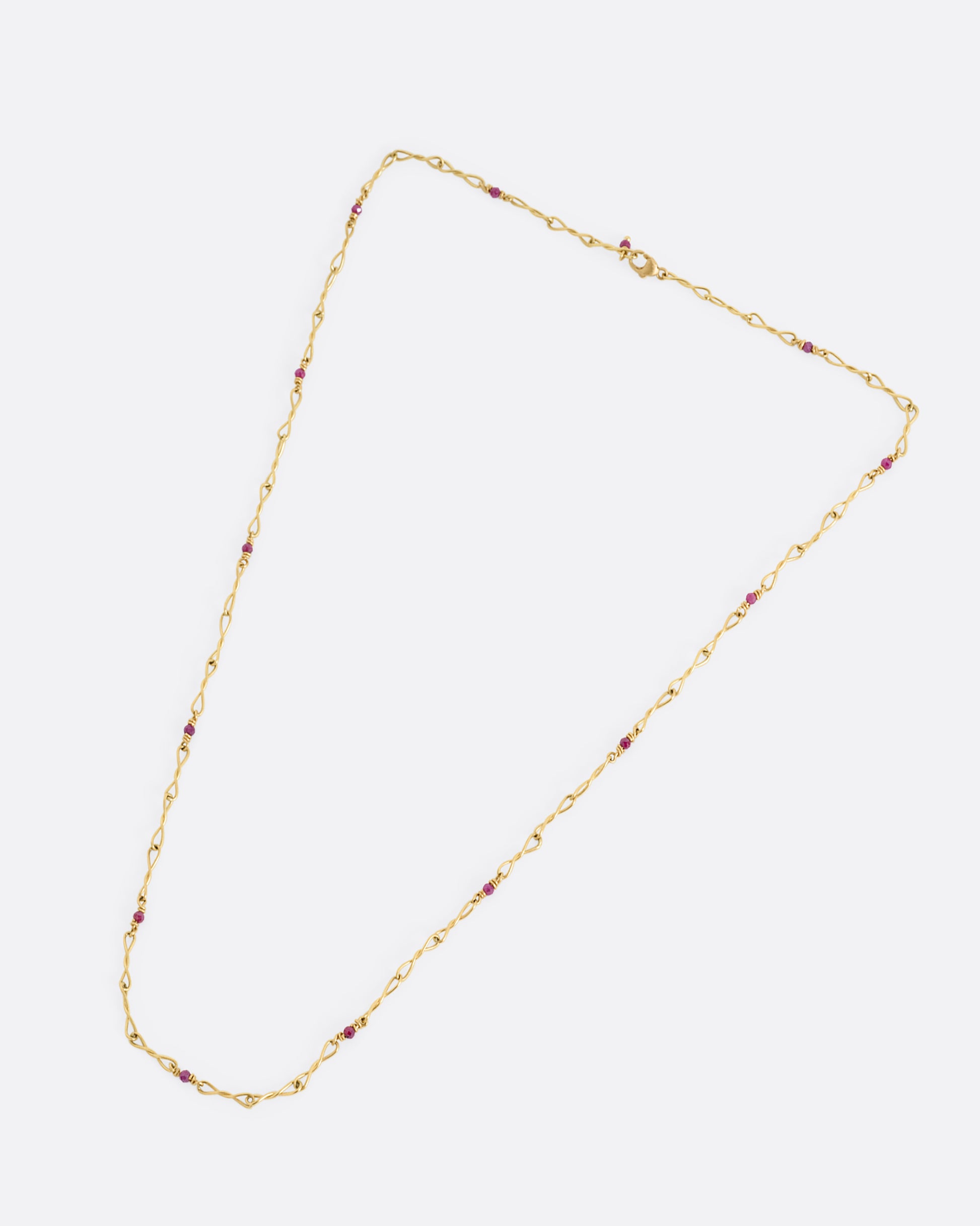 A yellow gold necklace with twisted links and ruby beads. Shown from the front.