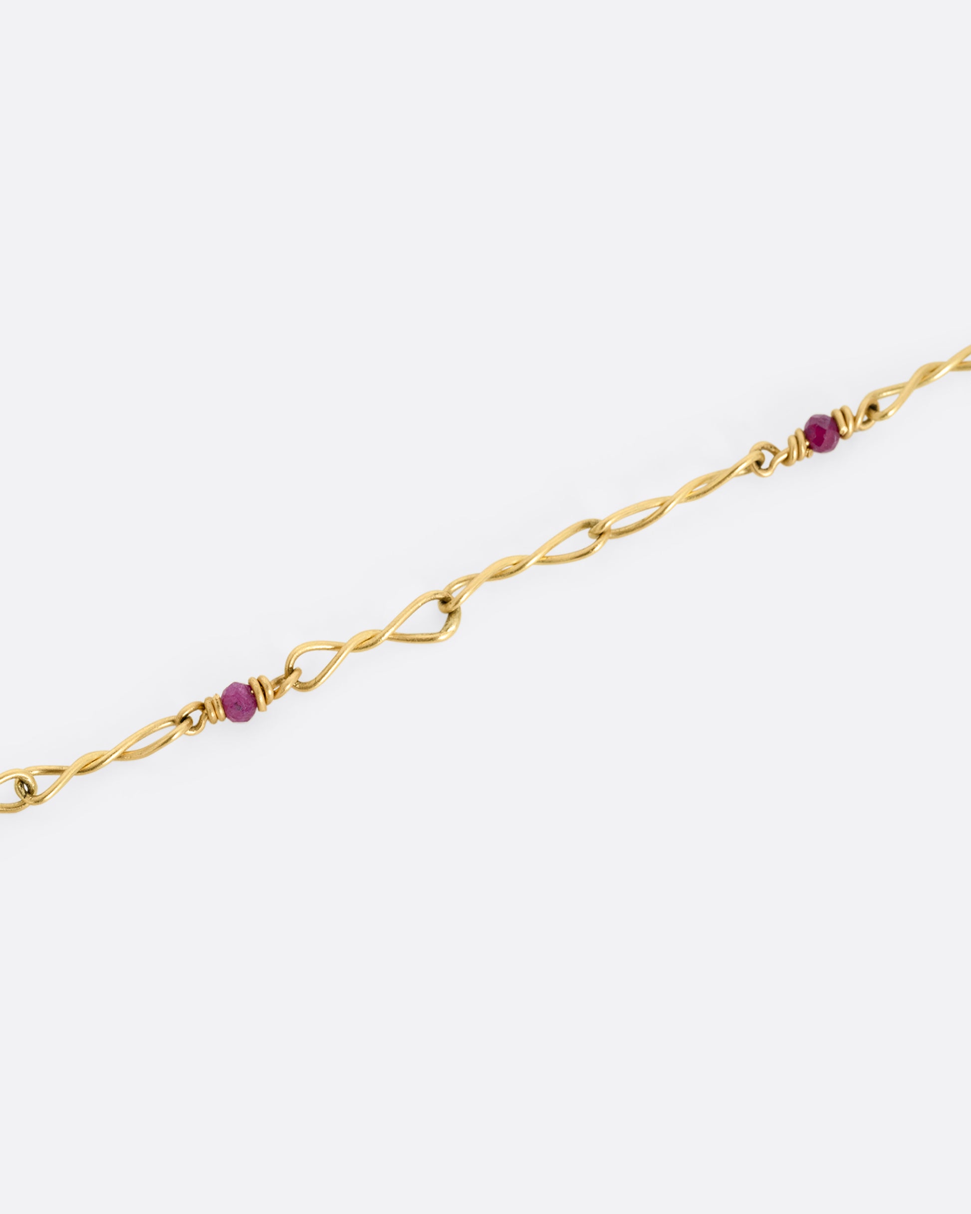 A yellow gold necklace with twisted links and ruby beads. Shown close up.