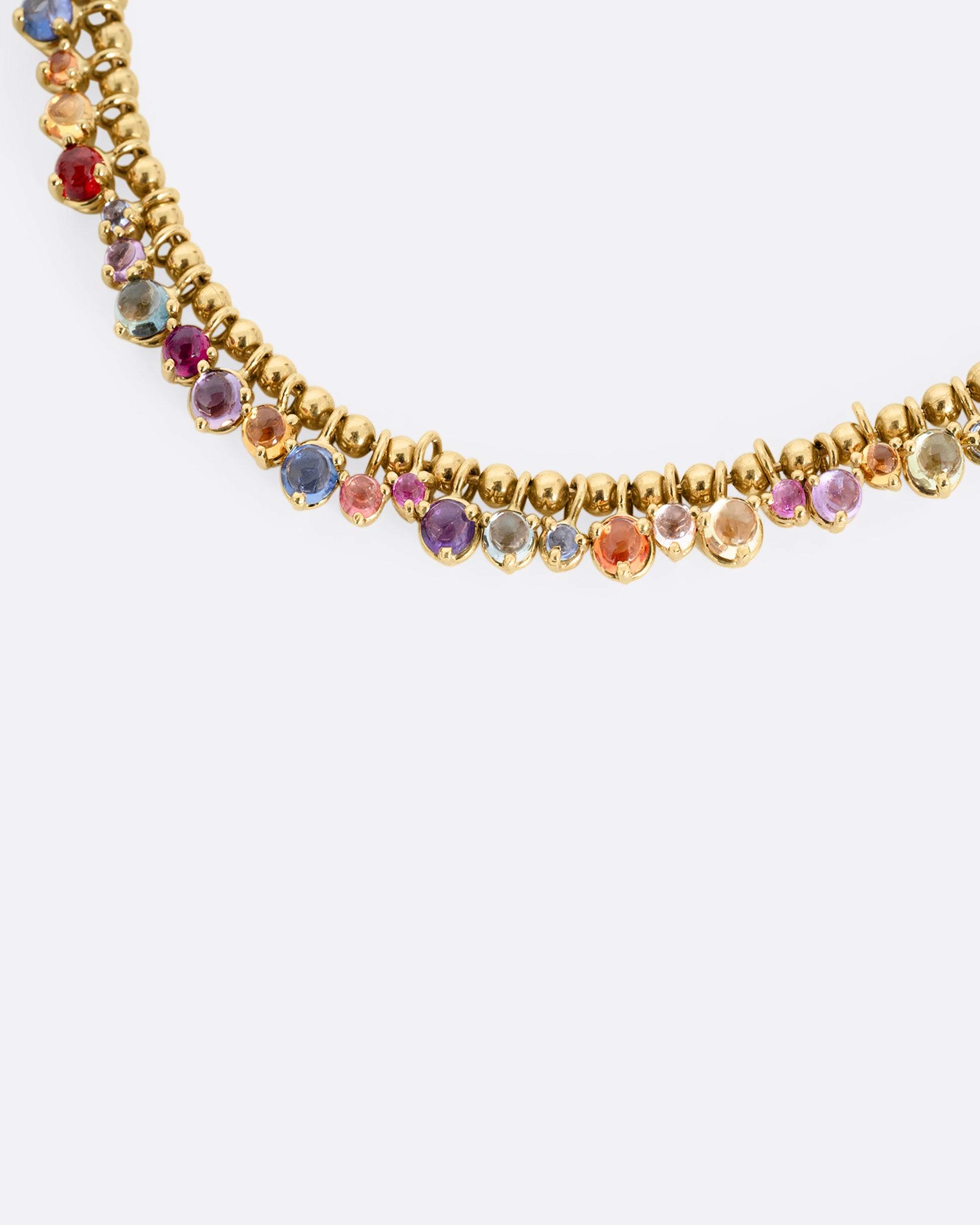 A close up of a yellow gold ball chain necklace with many multicolored sapphire dangles. Shown from the front.