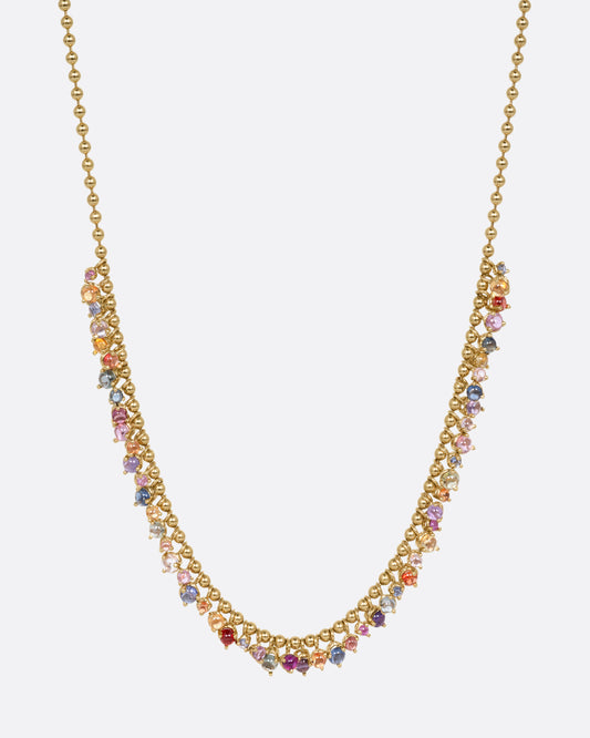 A yellow gold ball chain necklace with many multicolored sapphire dangles. Shown from the front.