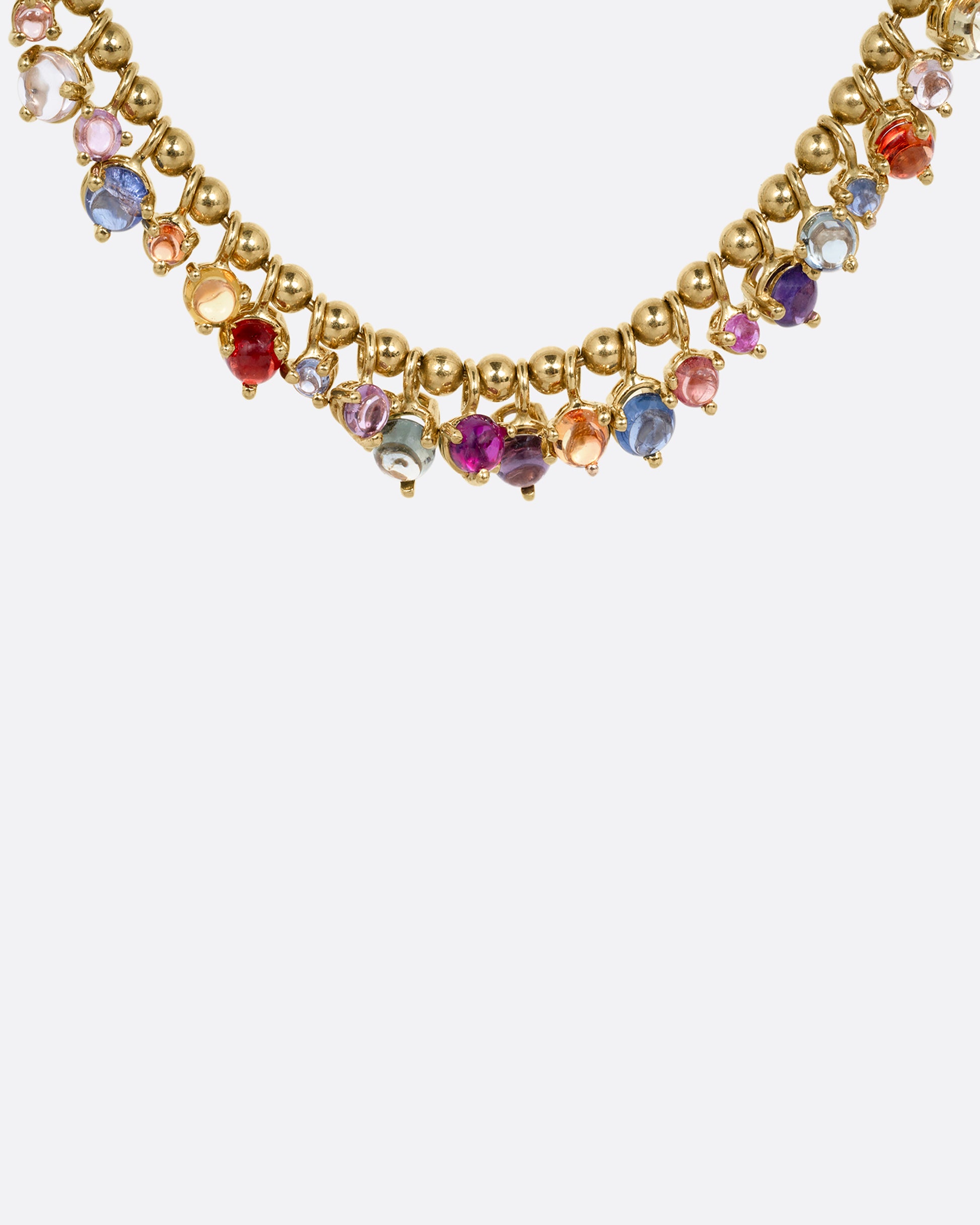 A close up of a yellow gold ball chain necklace with many multicolored sapphire dangles. Shown from the front.