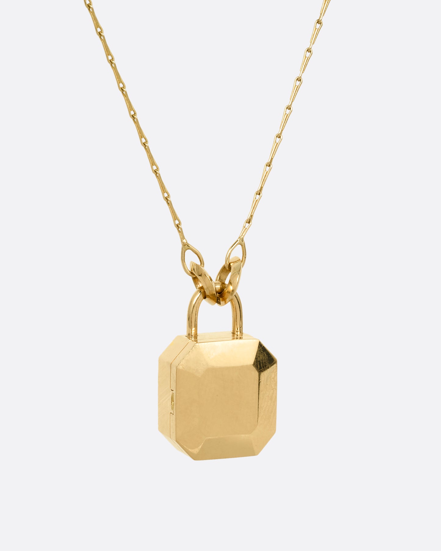 A yellow gold necklace with a padlock shaped locket pendant with multicolored sapphire on its face. Shown from the back.