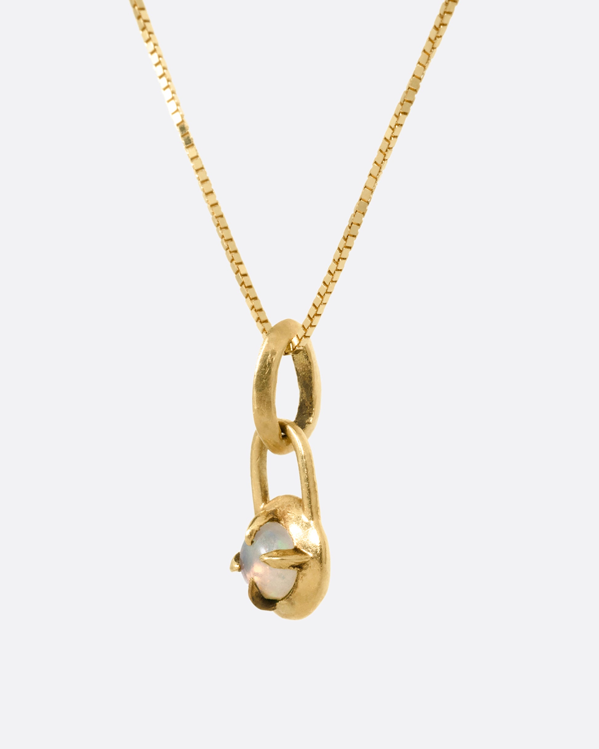A yellow gold box chain necklace with a prong set opal cabochon pendant, shown from the side.
