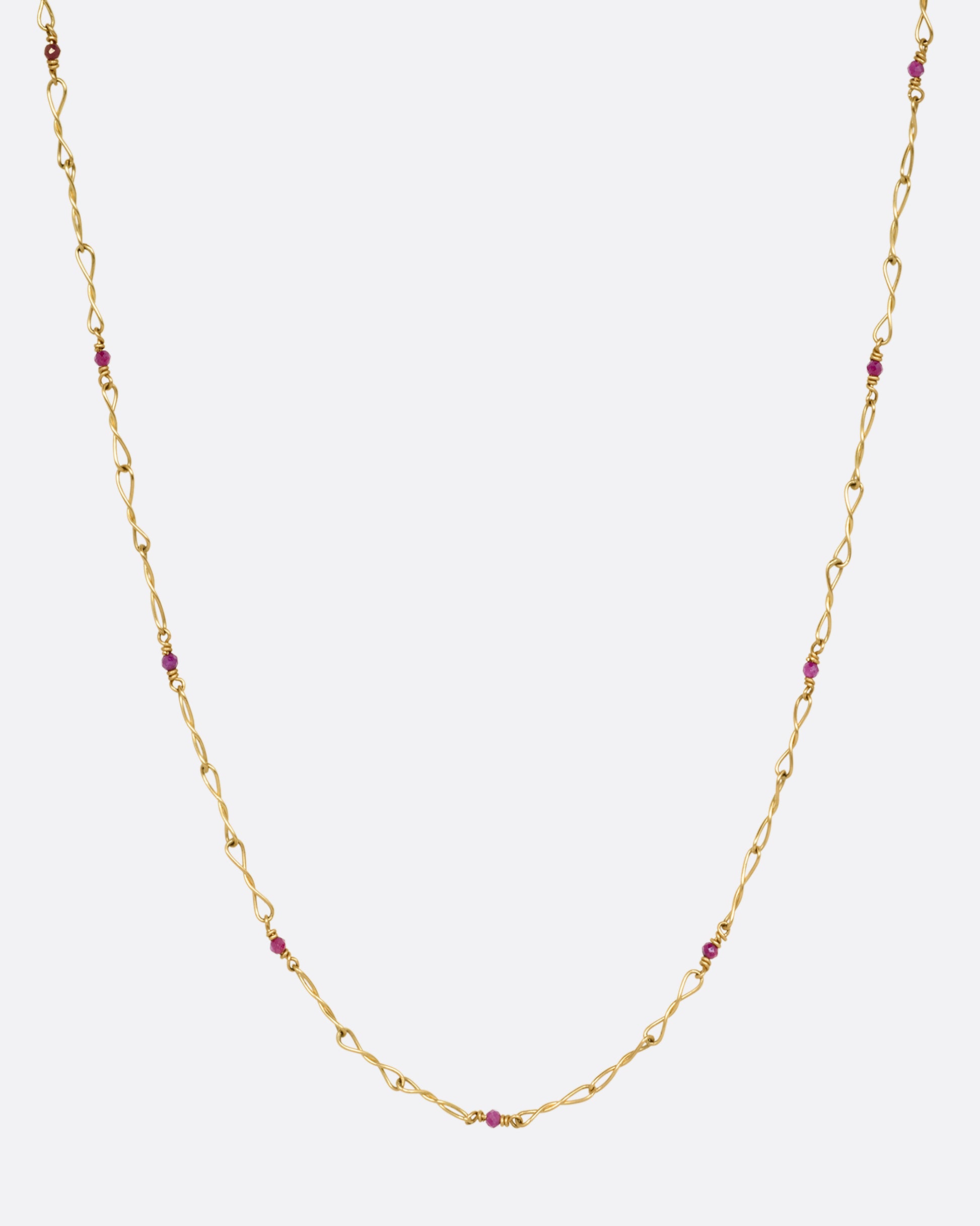 A yellow gold necklace with twisted links and ruby beads. Shown from the front.