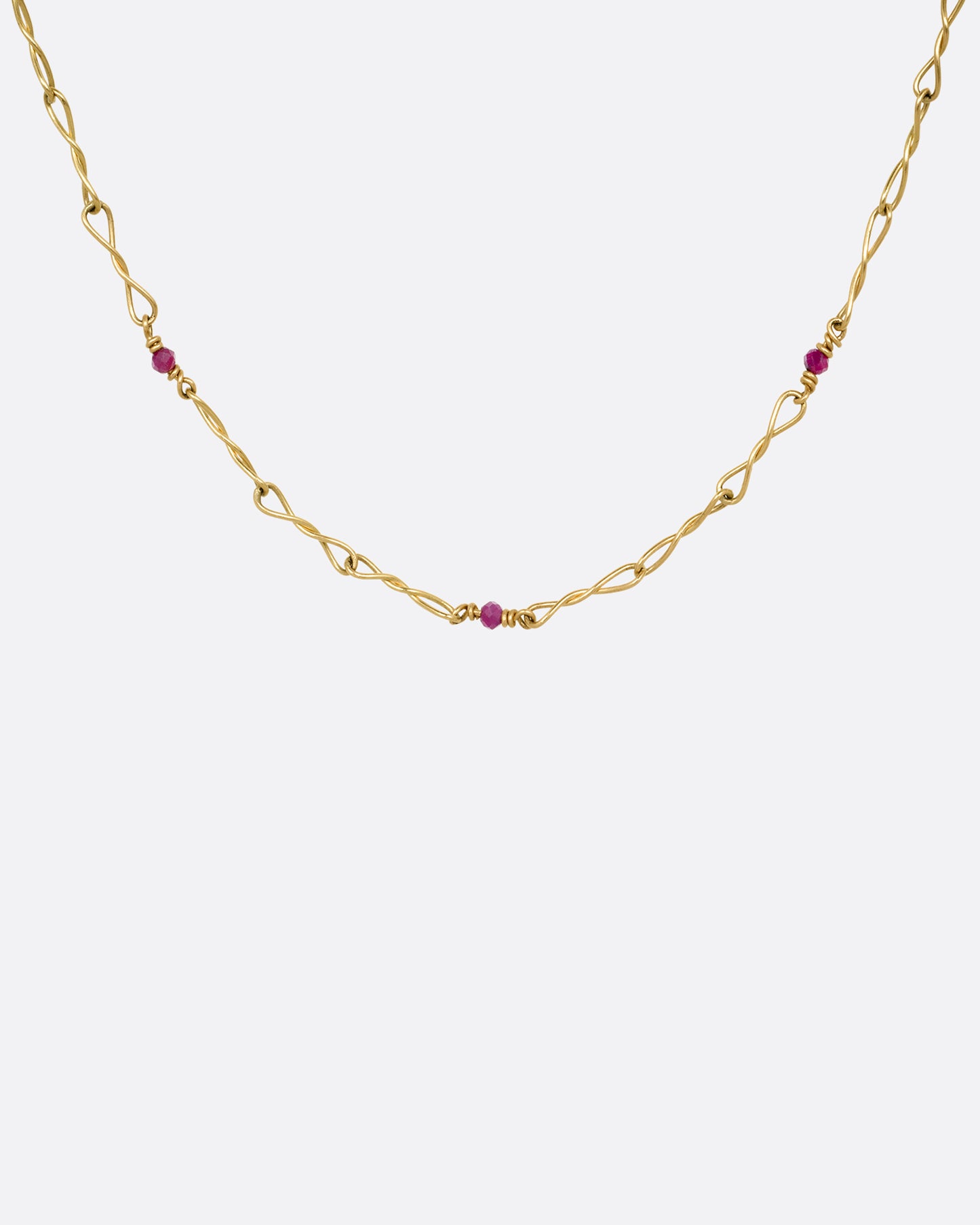 A yellow gold necklace with twisted links and ruby beads. Shown from the front.