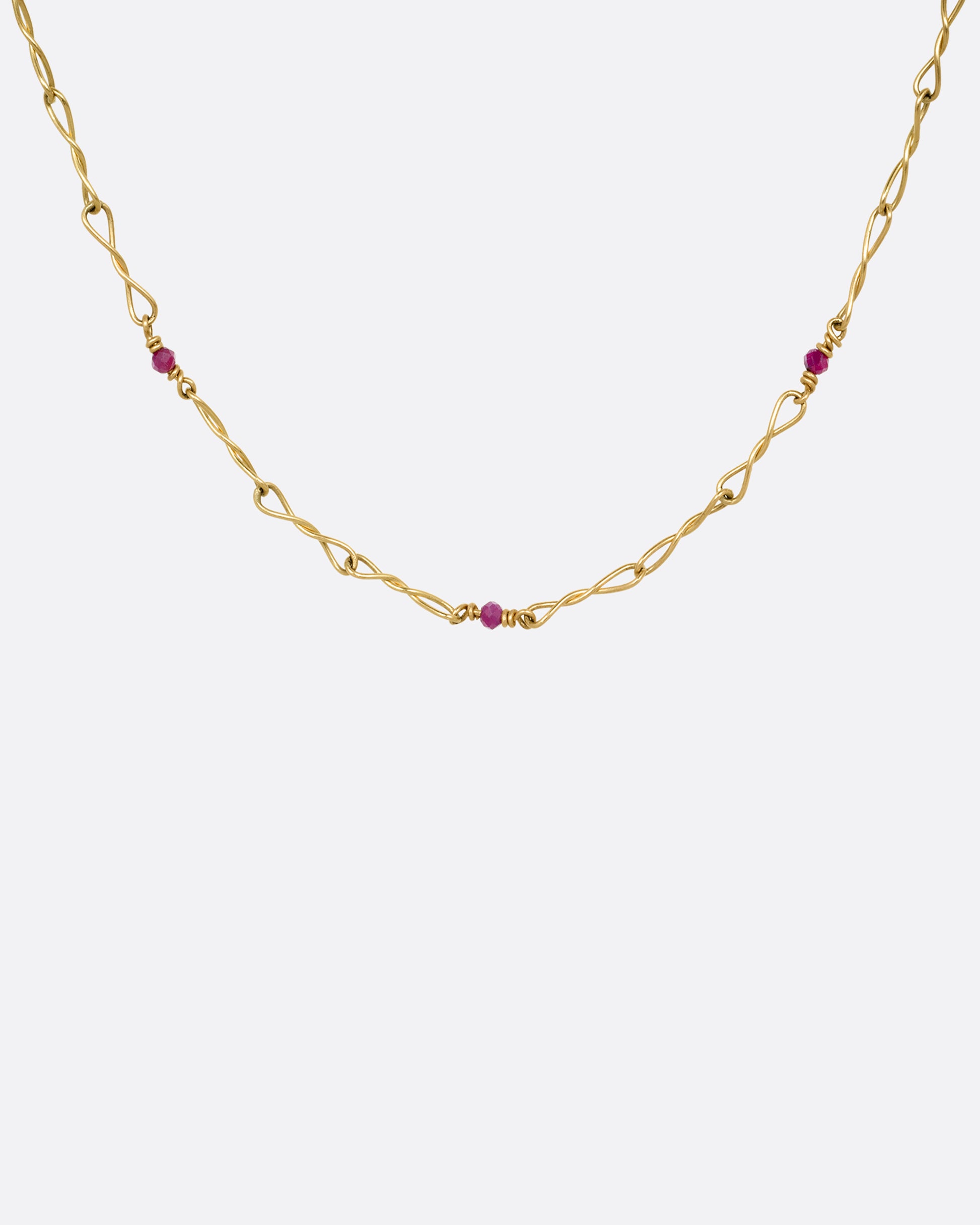 A yellow gold necklace with twisted links and ruby beads. Shown from the front.