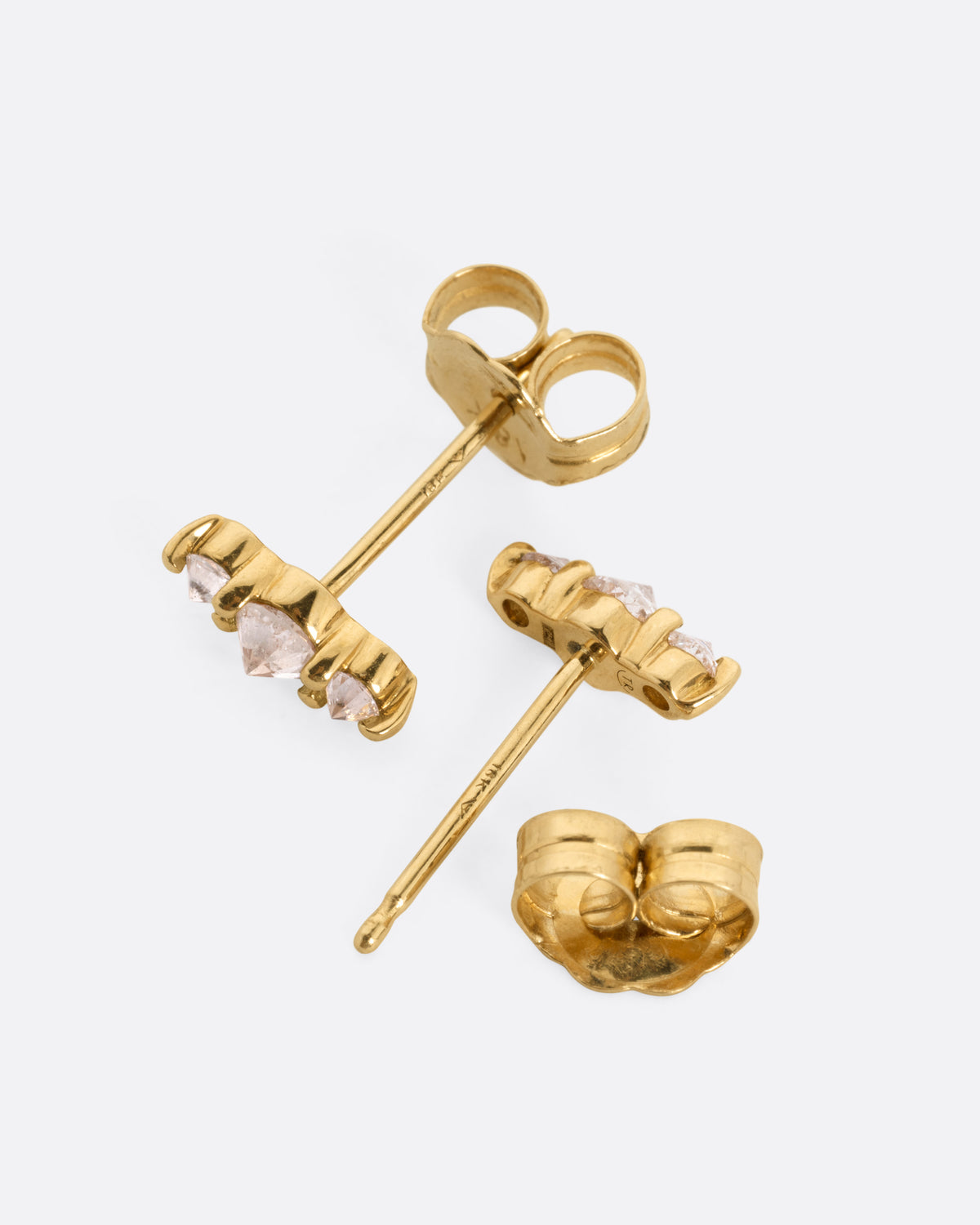 A pair of yellow gold stud earrings, each with three stacked diamonds, shown from the side with one earring open.