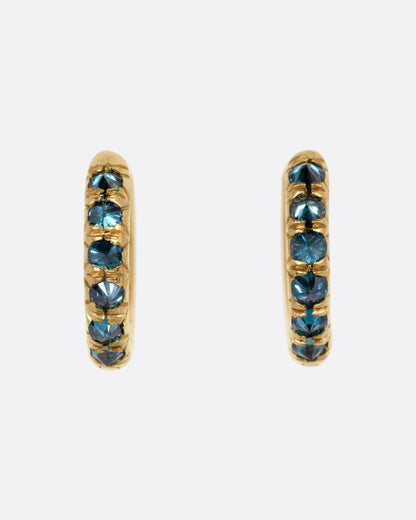 A pair of yellow gold huggie hoop earrings with reverse set blue diamonds, shown from the front.