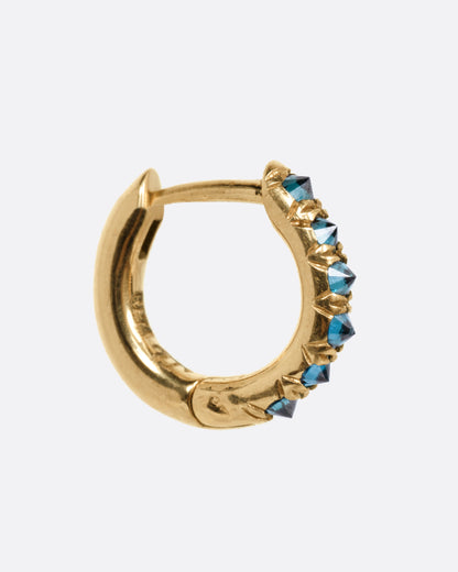 A yellow gold huggie hoop earring with reverse set blue diamonds, shown from the side.