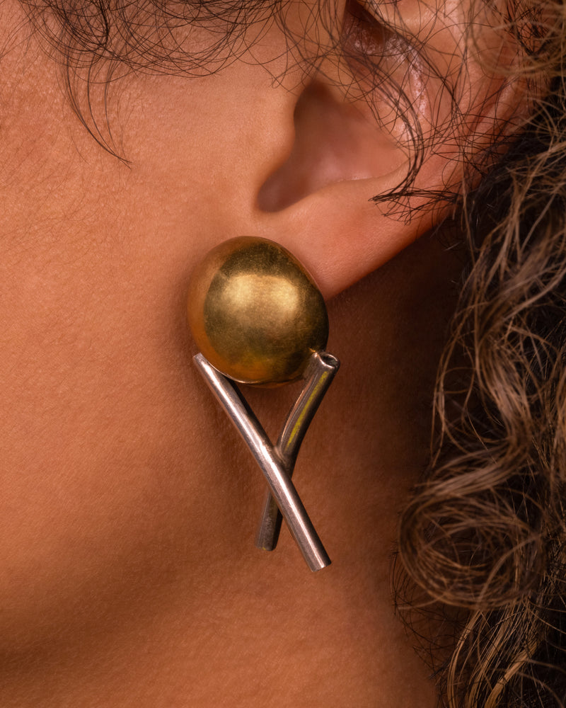 Vintage stud earring in sterling silver and brass worn on an ear, a brass dome resting on two crossed silver tubes