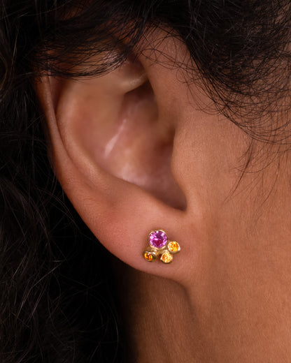 A yellow gold stud earring with a pink and orange sapphire cluster, shown on a person.