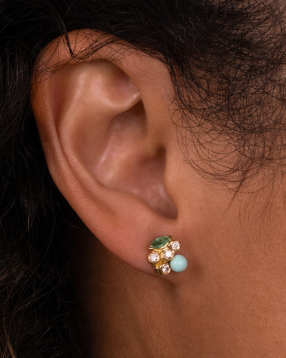A yellow gold stud earring with diamonds, emeralds, and turquoise, shown on a person.