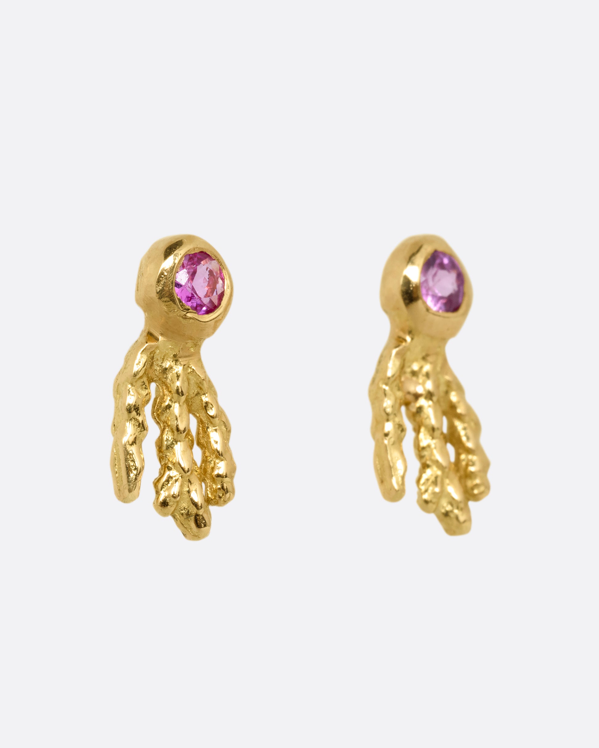 A pair of yellow gold earrings with pink sapphires and gold kelp- like tails. Shown from the side.