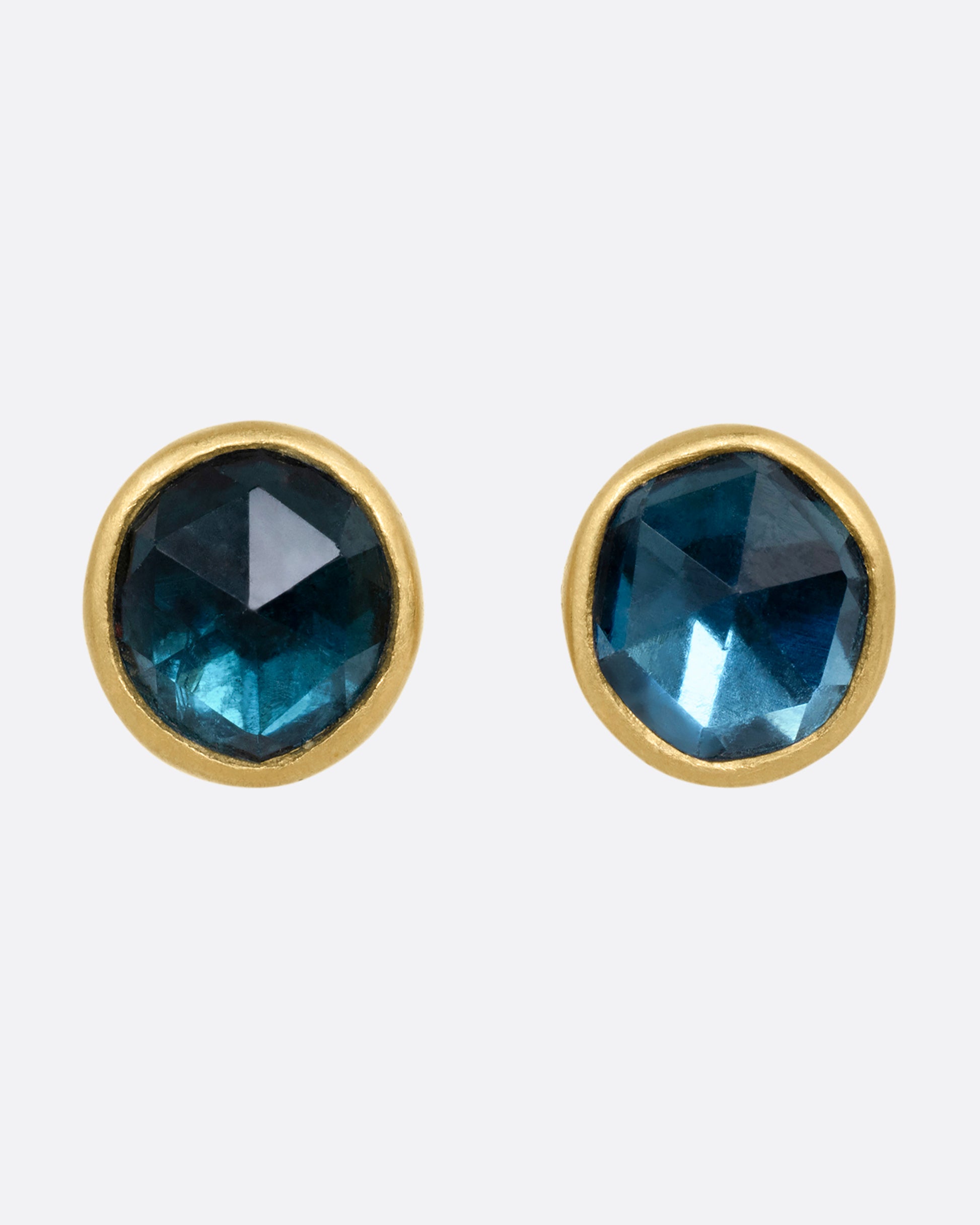 A pair of yellow gold stud earrings with blue green tourmalines. Shown from the front.