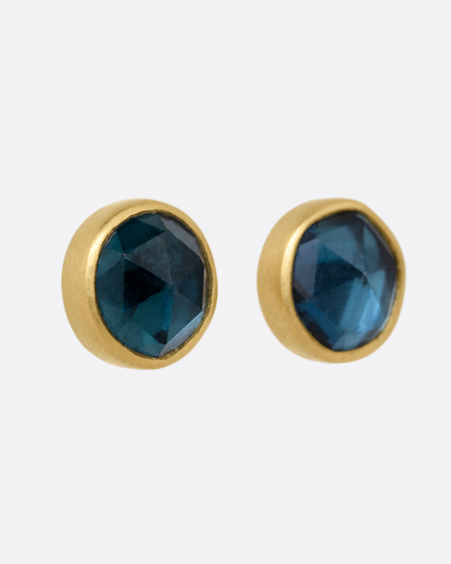 A pair of yellow gold stud earrings with blue green tourmalines. Shown from the side.