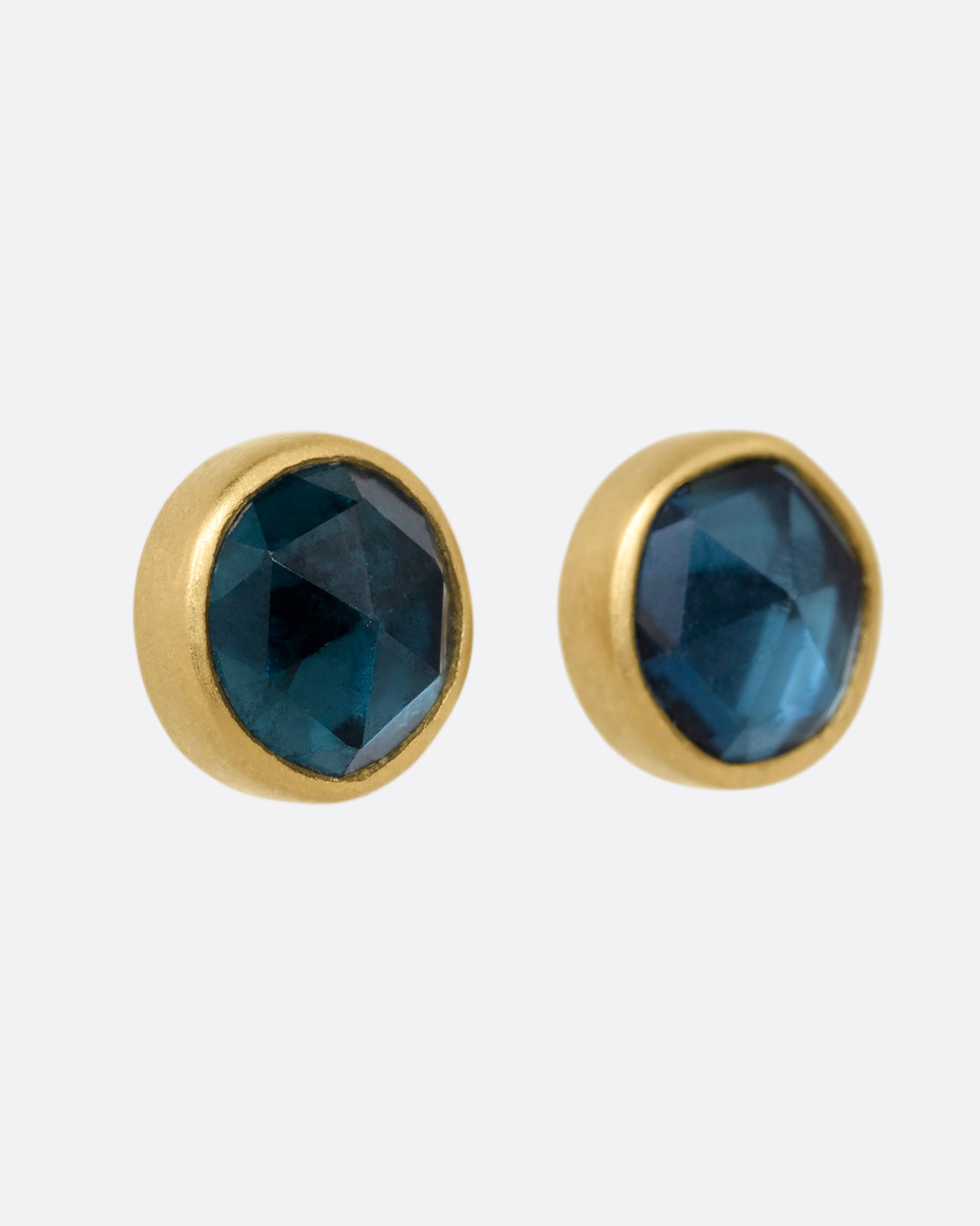 A pair of yellow gold stud earrings with blue green tourmalines. Shown from the side.