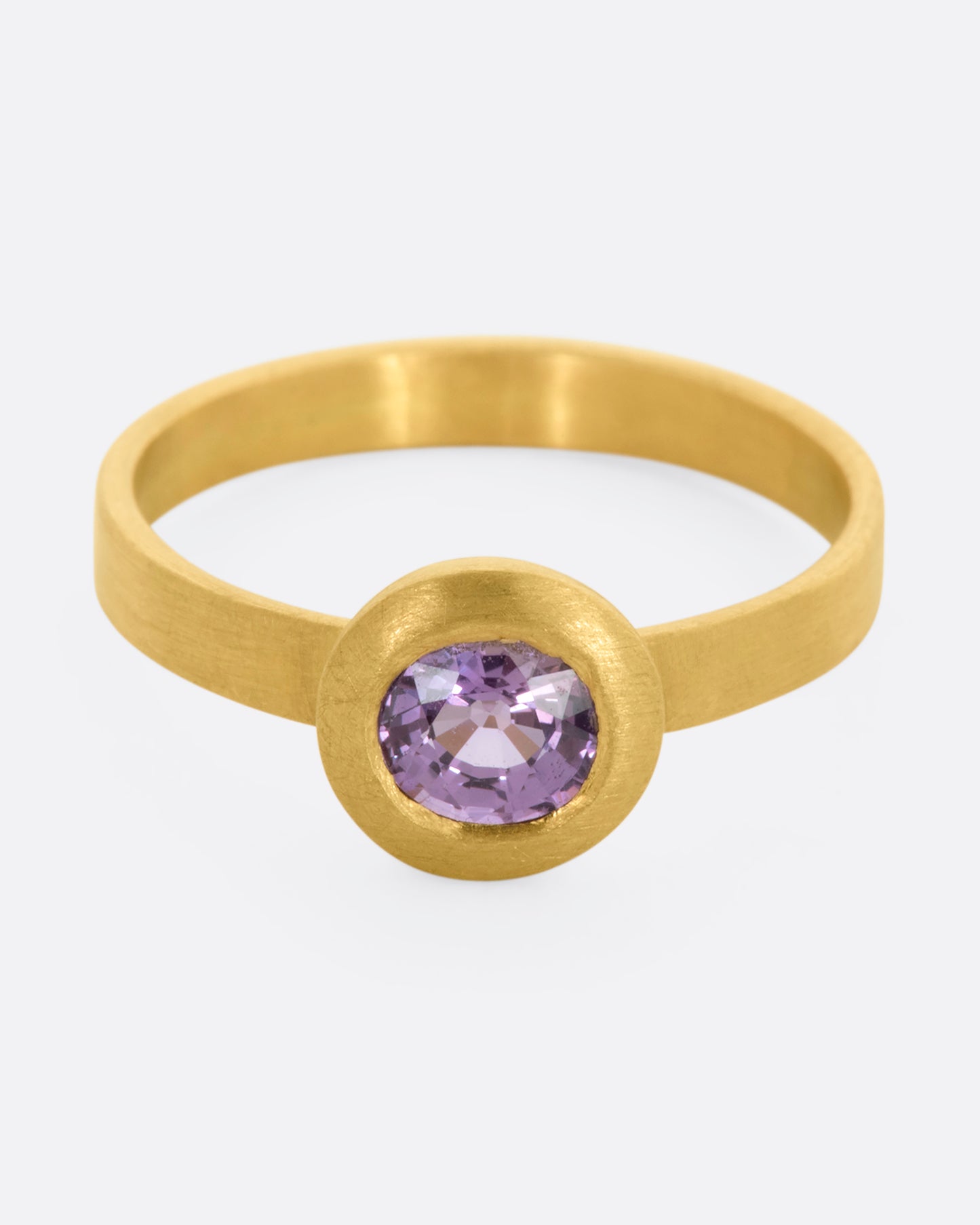 A yellow gold ring with a purple sapphire. Shown from the front, slightly above.