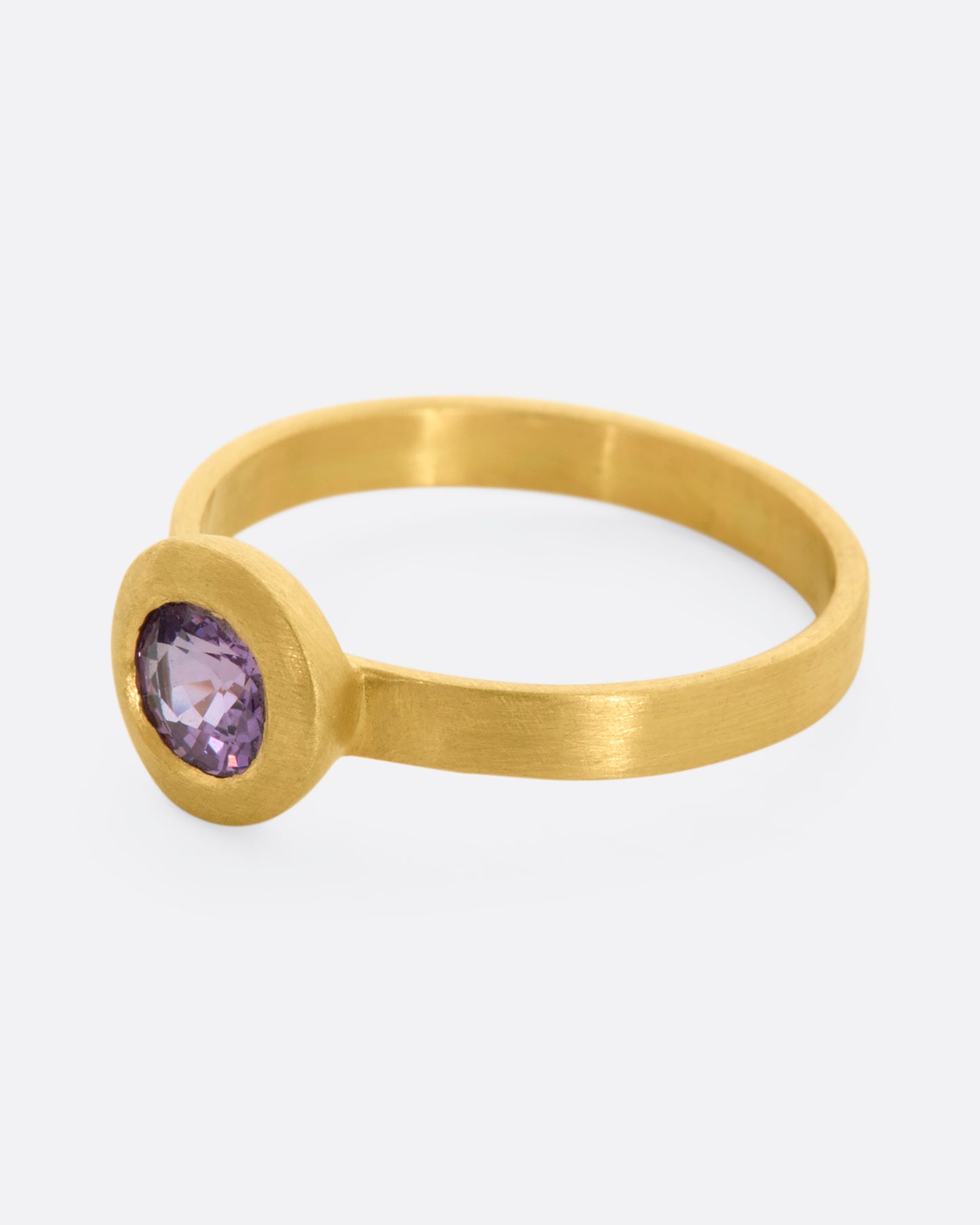 A yellow gold ring with a purple sapphire. Shown from the side.