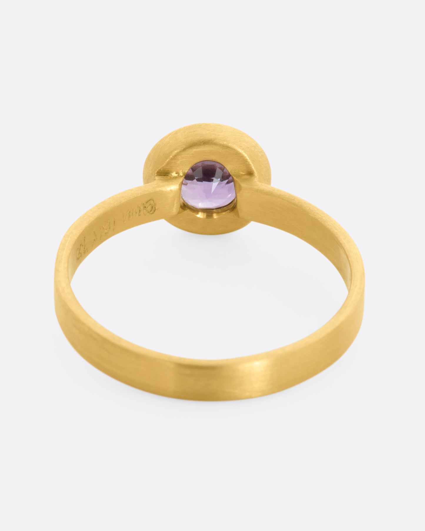 A yellow gold ring with a purple sapphire. Shown from the back.