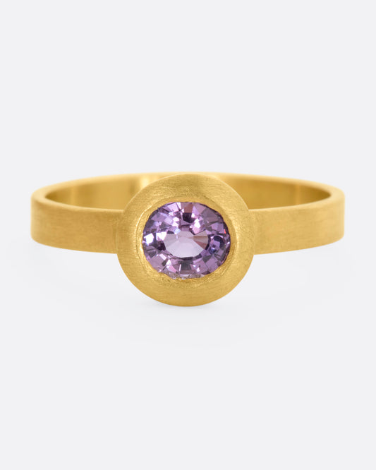 A yellow gold ring with a purple sapphire. Shown from the front.