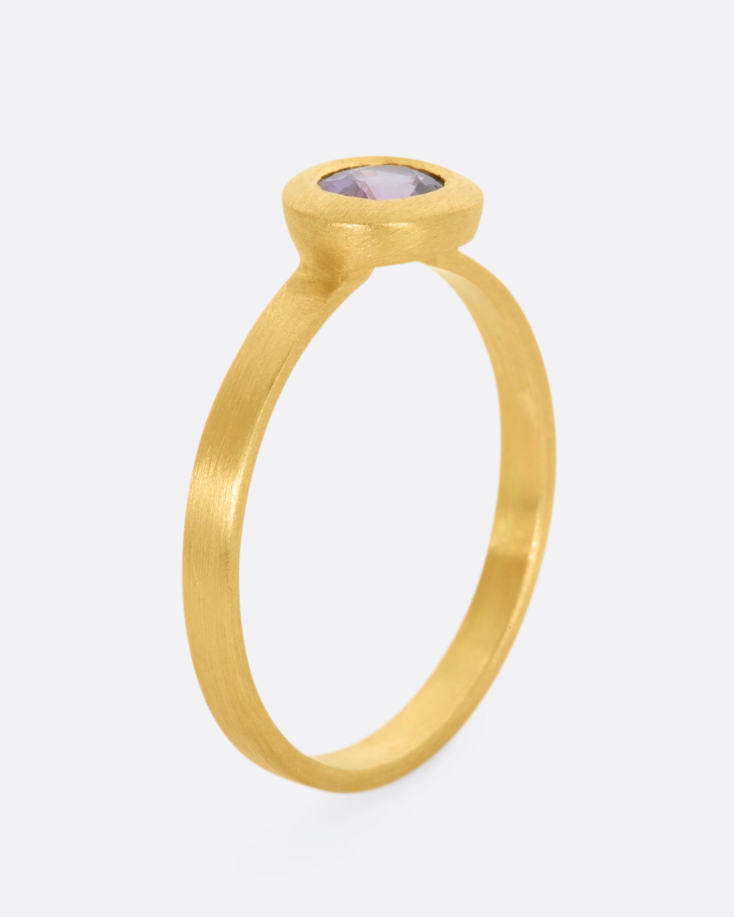 A yellow gold ring with a purple sapphire. Shown from the side, standing up.