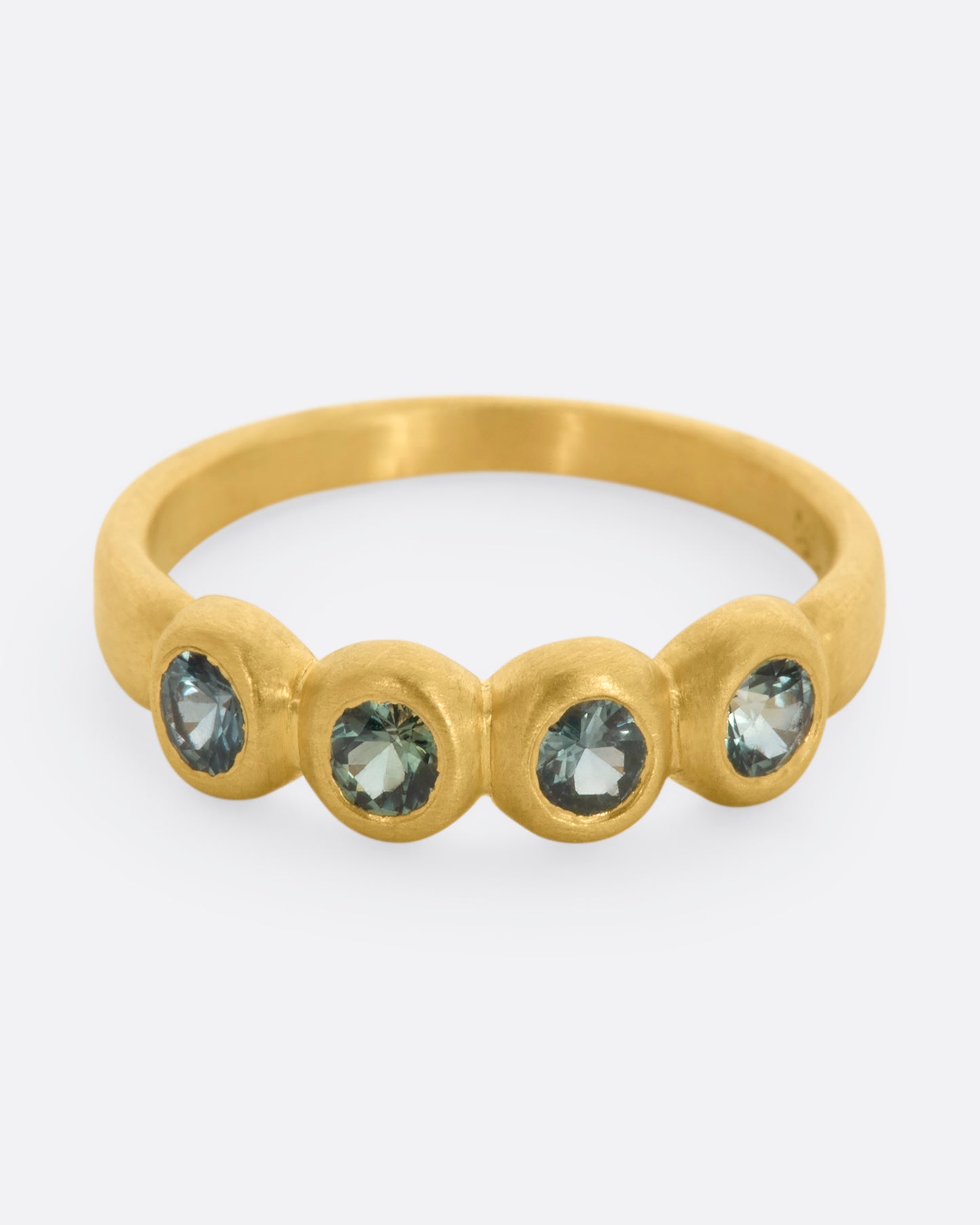 A yellow gold band with a row of four green sapphires. Shown from the front, from slightly above.