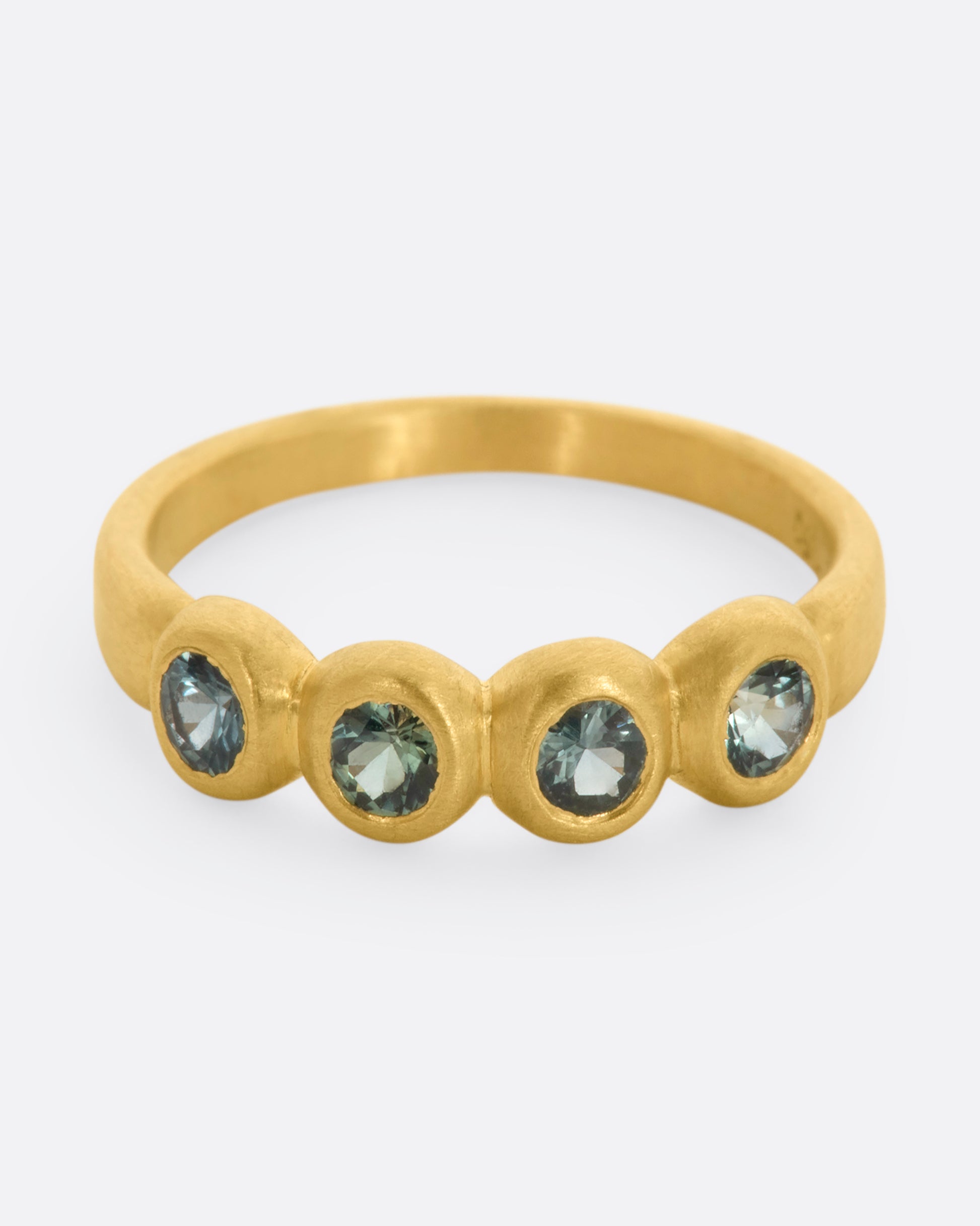 A yellow gold band with a row of four green sapphires. Shown from the front, from slightly above.