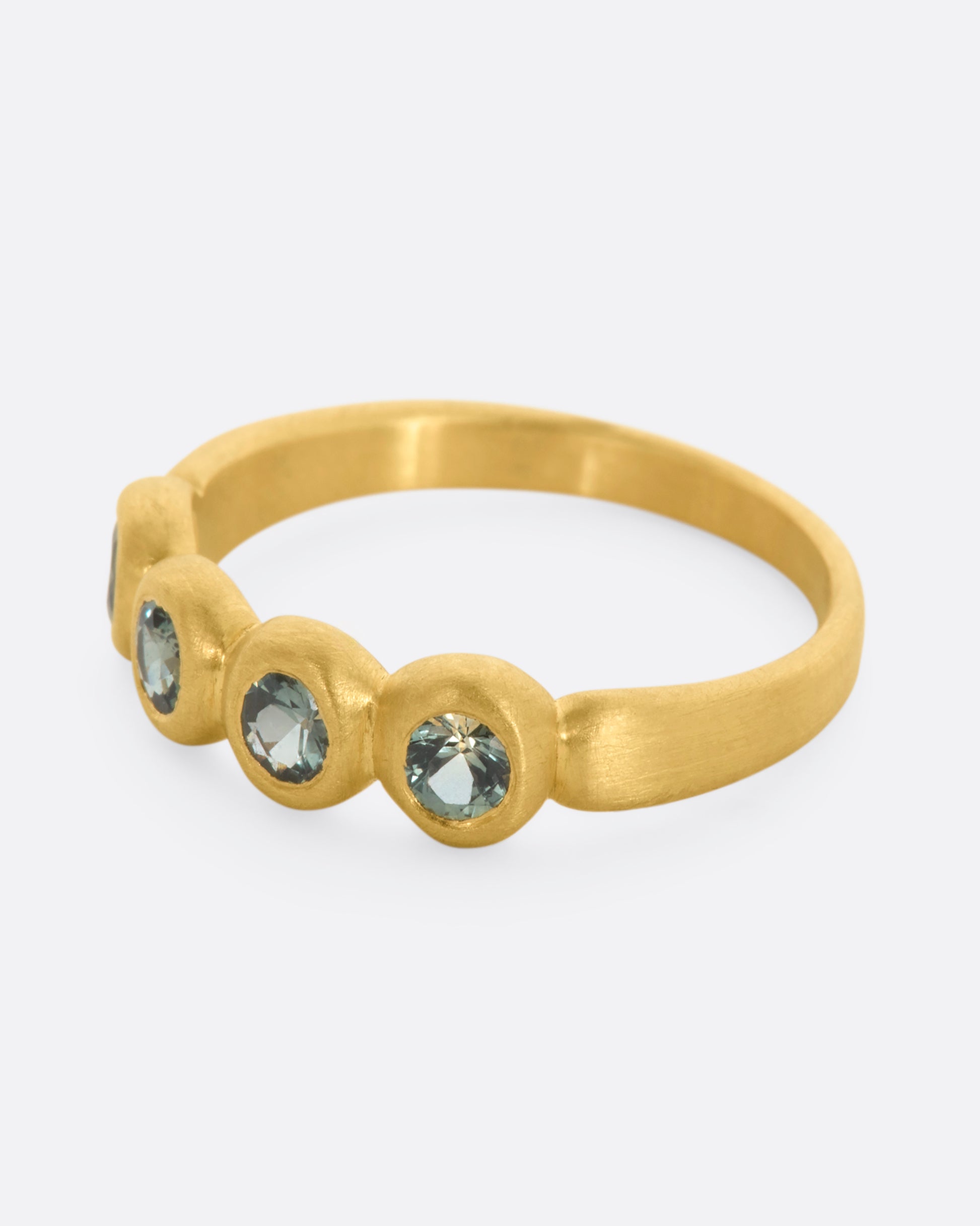 A yellow gold band with a row of four green sapphires. Shown from the side.