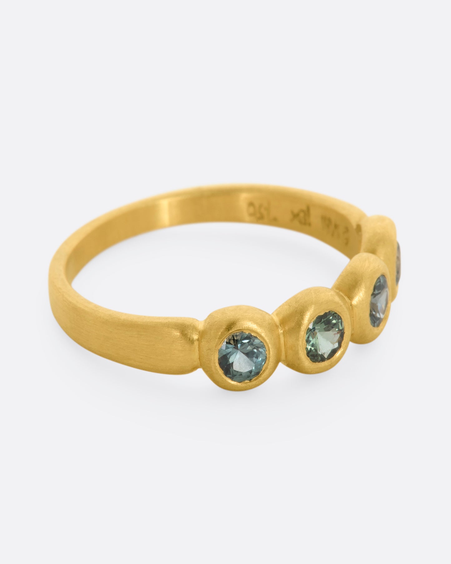 A yellow gold band with a row of four green sapphires. Shown from the side.