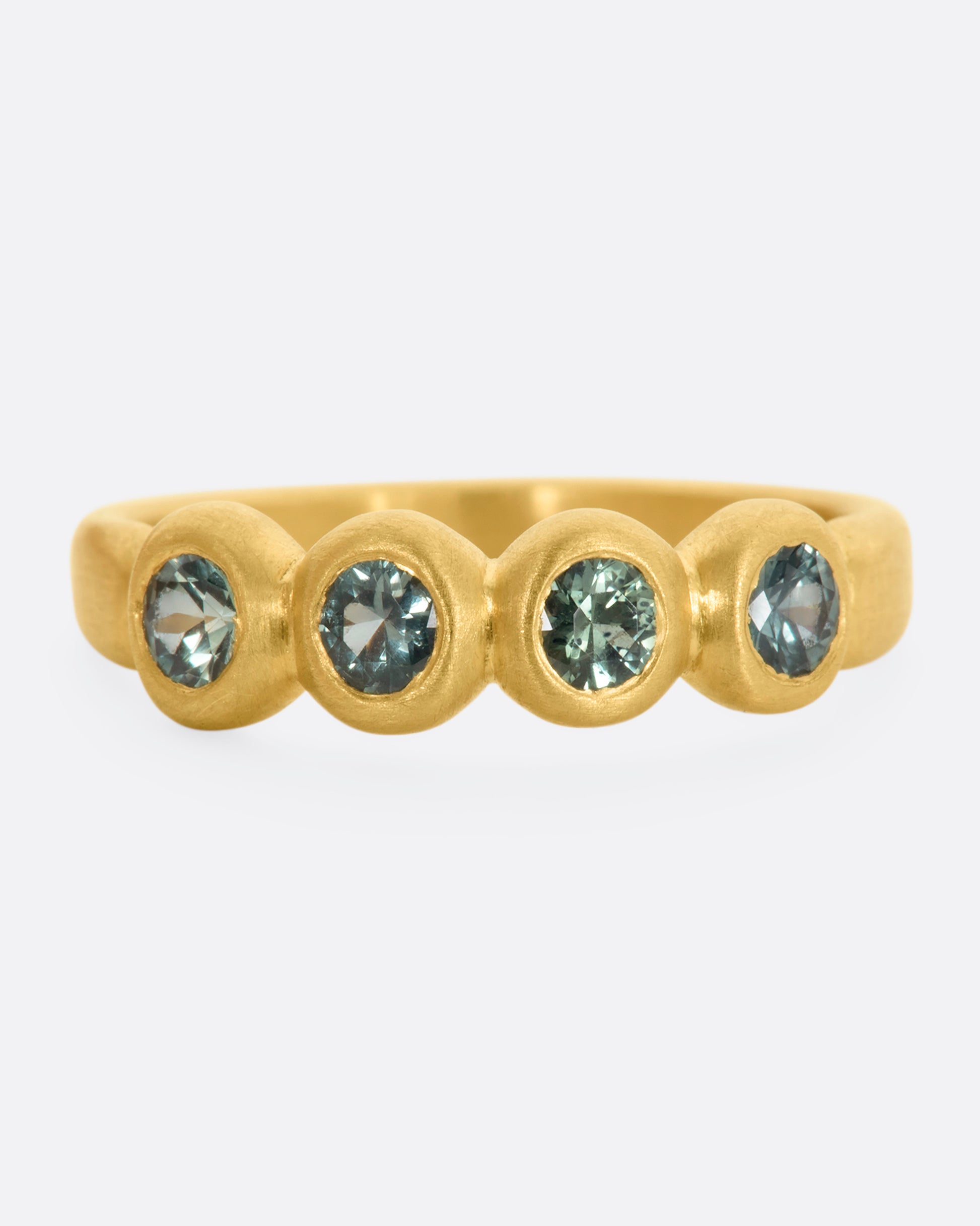 A yellow gold band with a row of four green sapphires. Shown from the front.