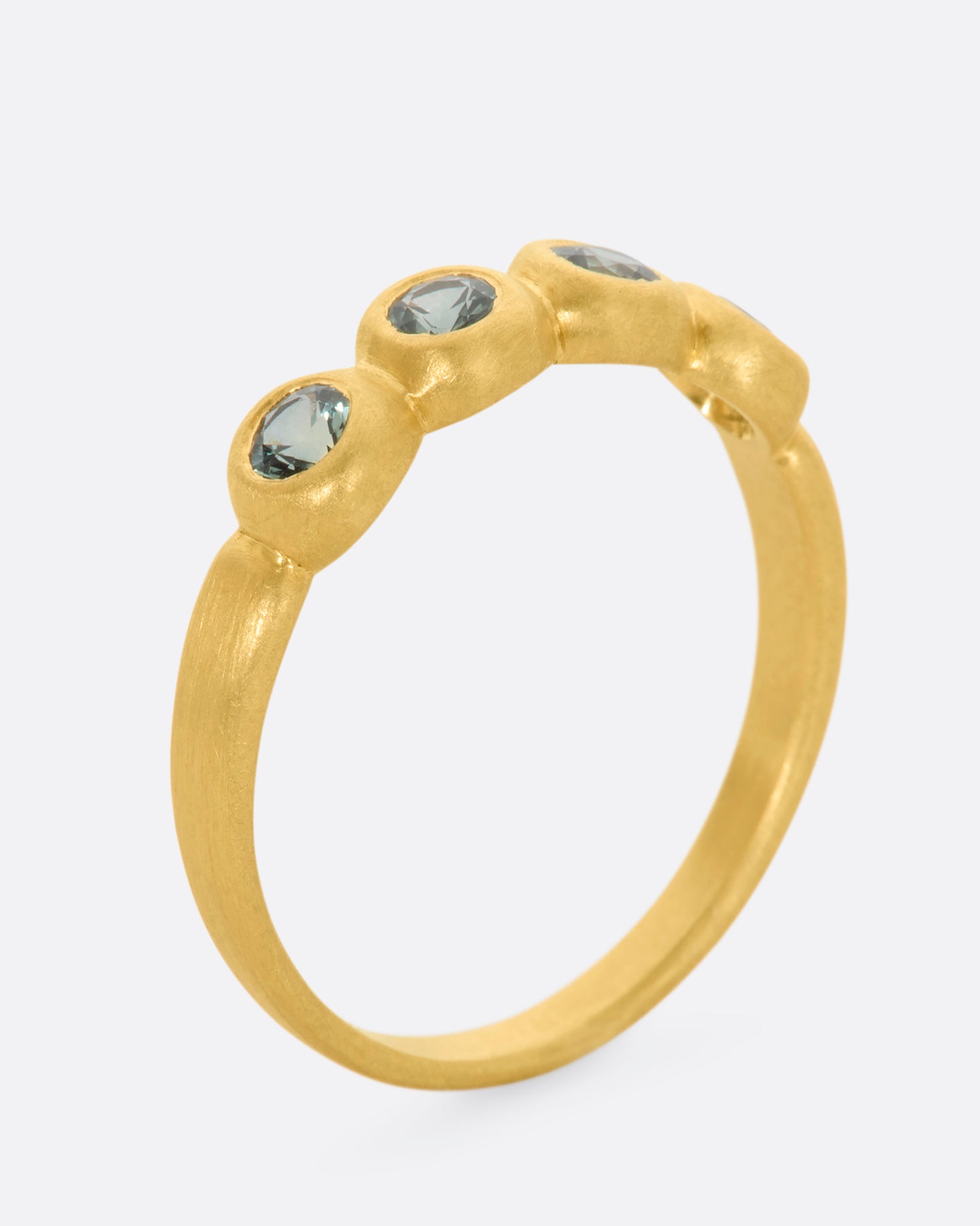 A yellow gold band with a row of four green sapphires. Shown from the side, standing up.