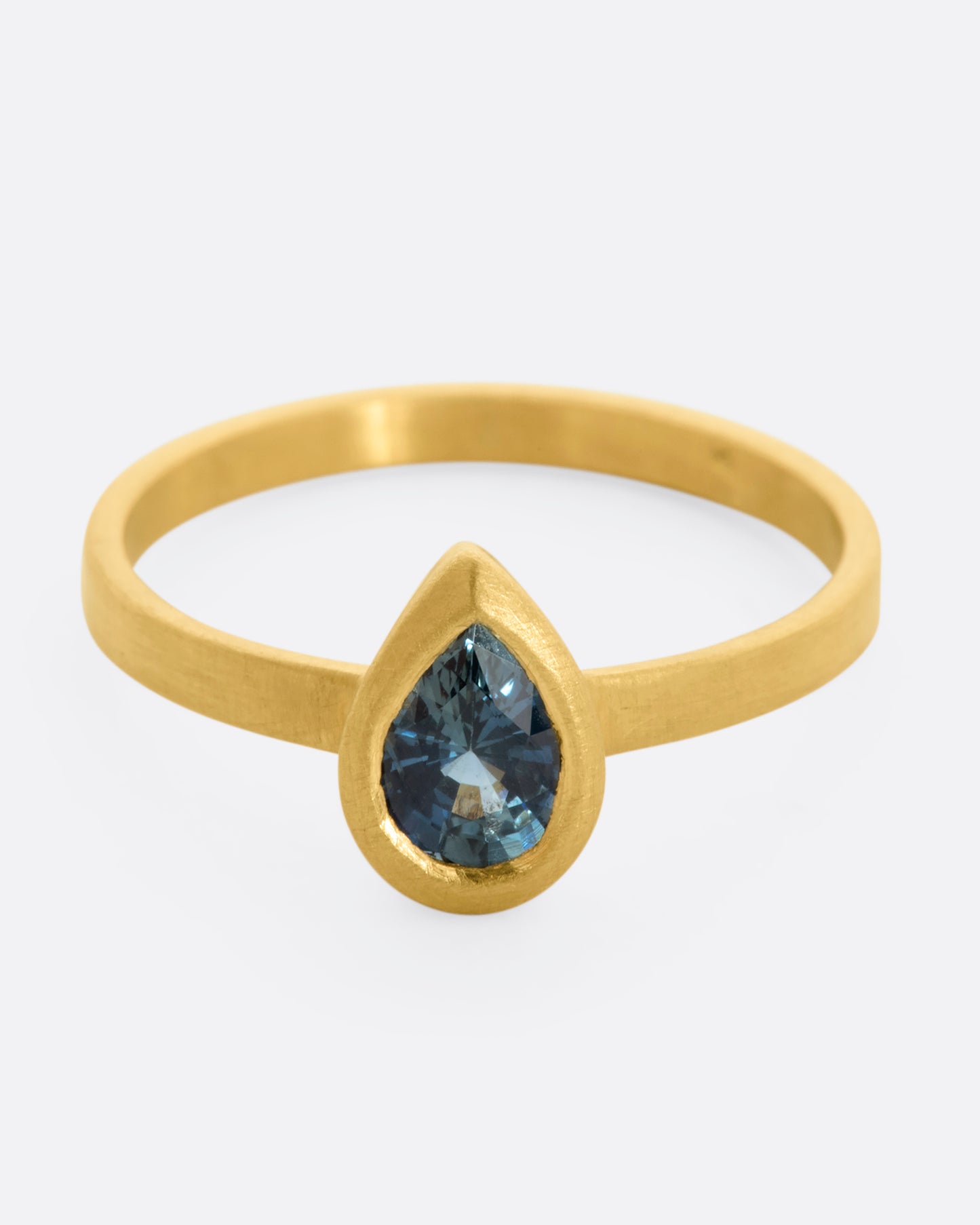 A yellow gold ring with a teal teardrop shaped sapphire. Shown from the front, slightly above.