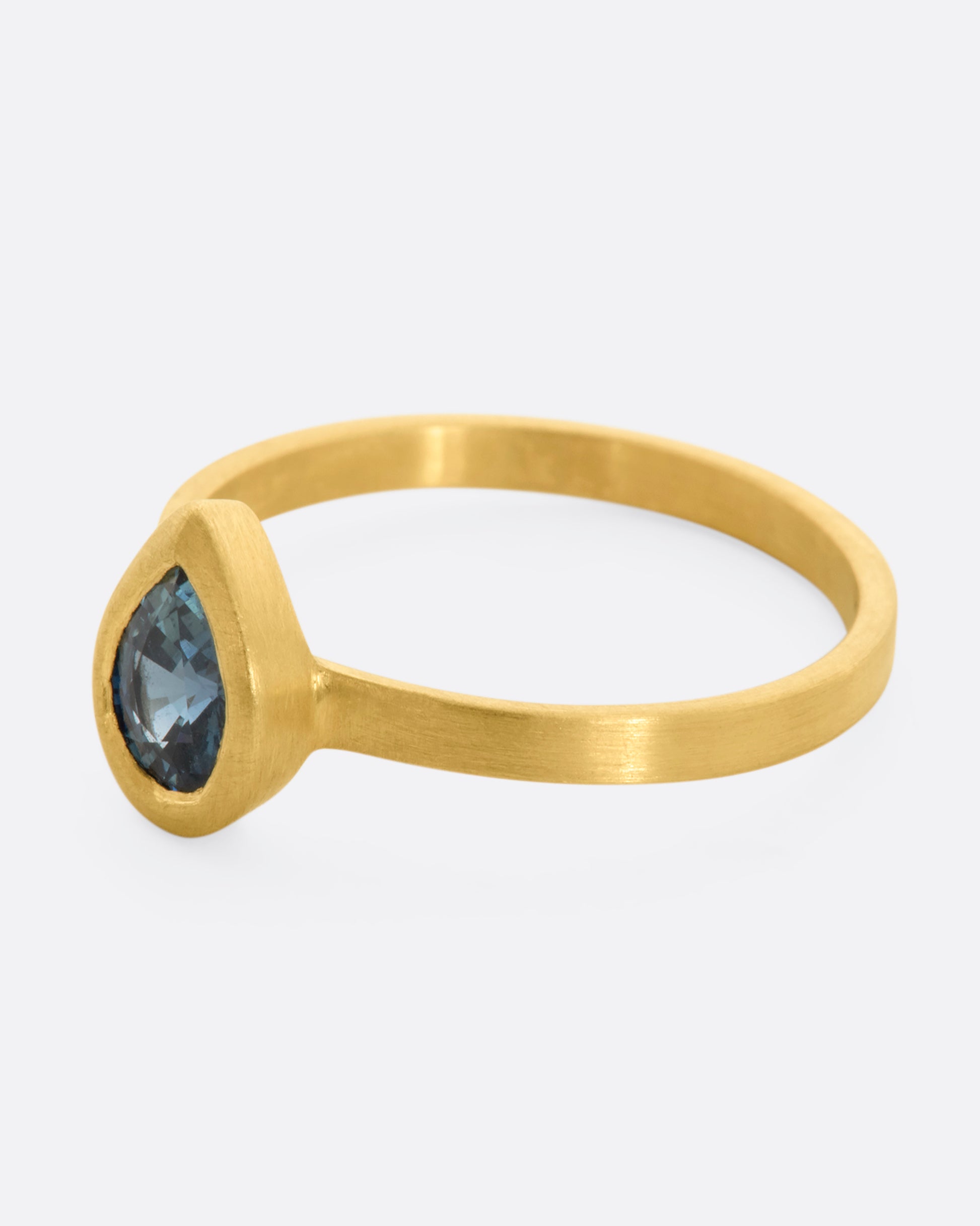 A yellow gold ring with a teal teardrop shaped sapphire. Shown from the side.