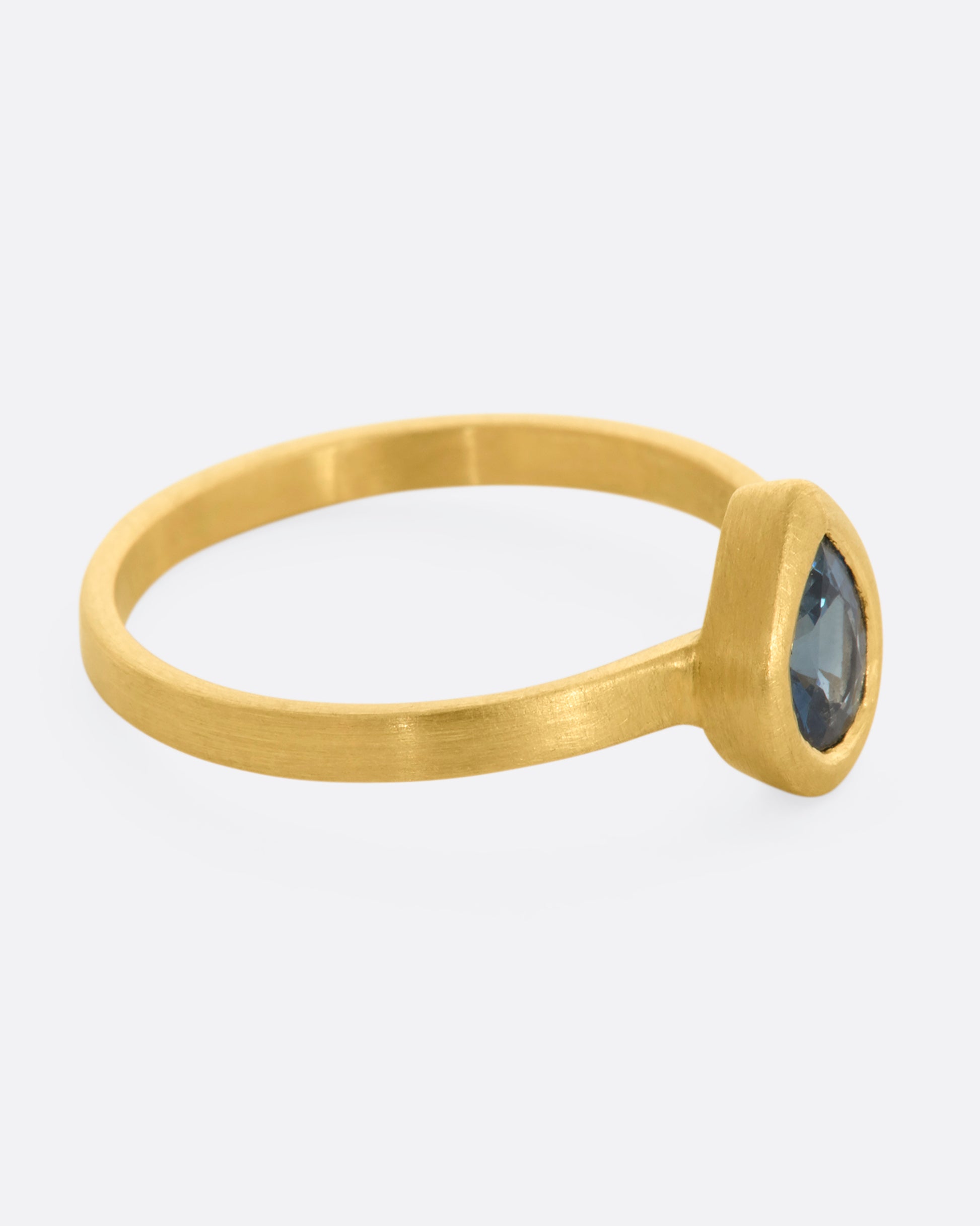 A yellow gold ring with a teal teardrop shaped sapphire. Shown from the side.