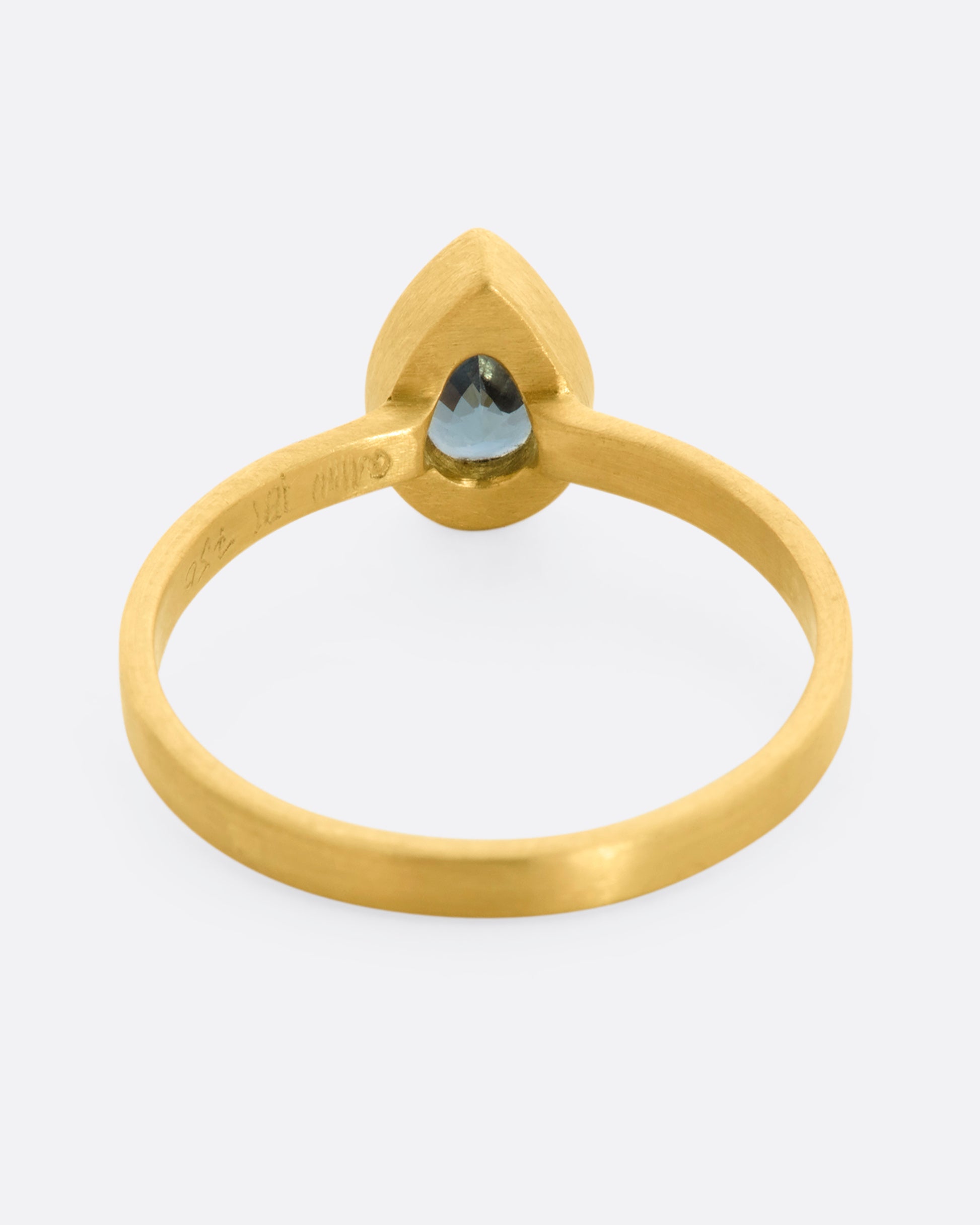 A yellow gold ring with a teal teardrop shaped sapphire. Shown from the back.