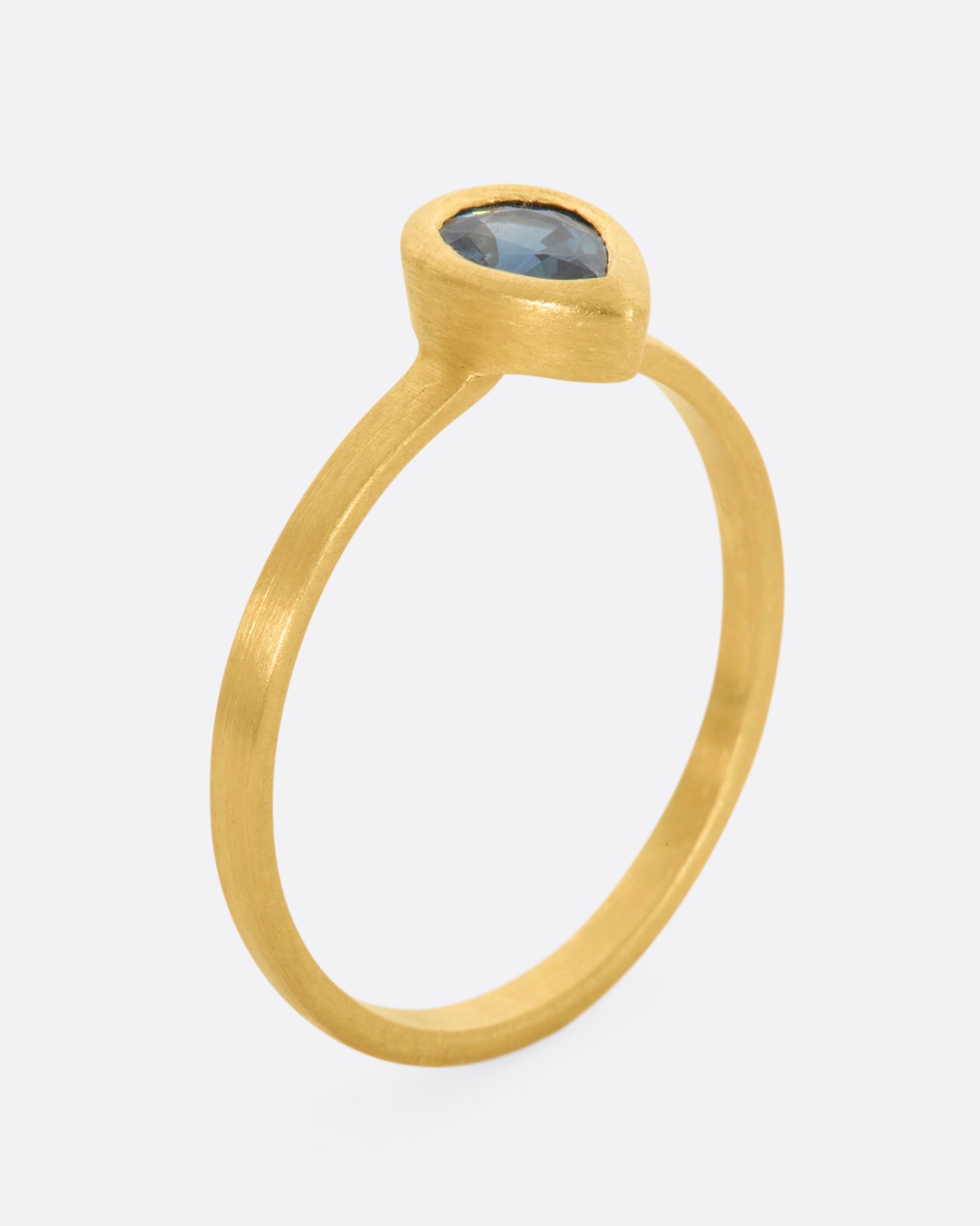 A yellow gold ring with a teal teardrop shaped sapphire. Shown from the side, standing up.