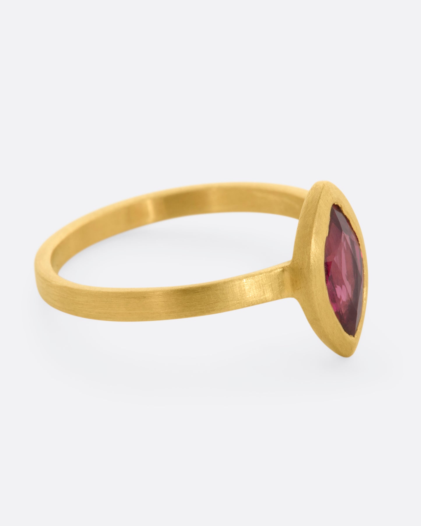 A matte yellow gold ring with a bezel set ruby marquise. View from the alternate side.