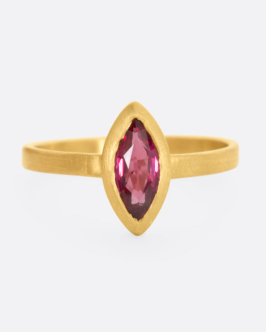 A matte yellow gold ring with a bezel set ruby marquise. View from the front.