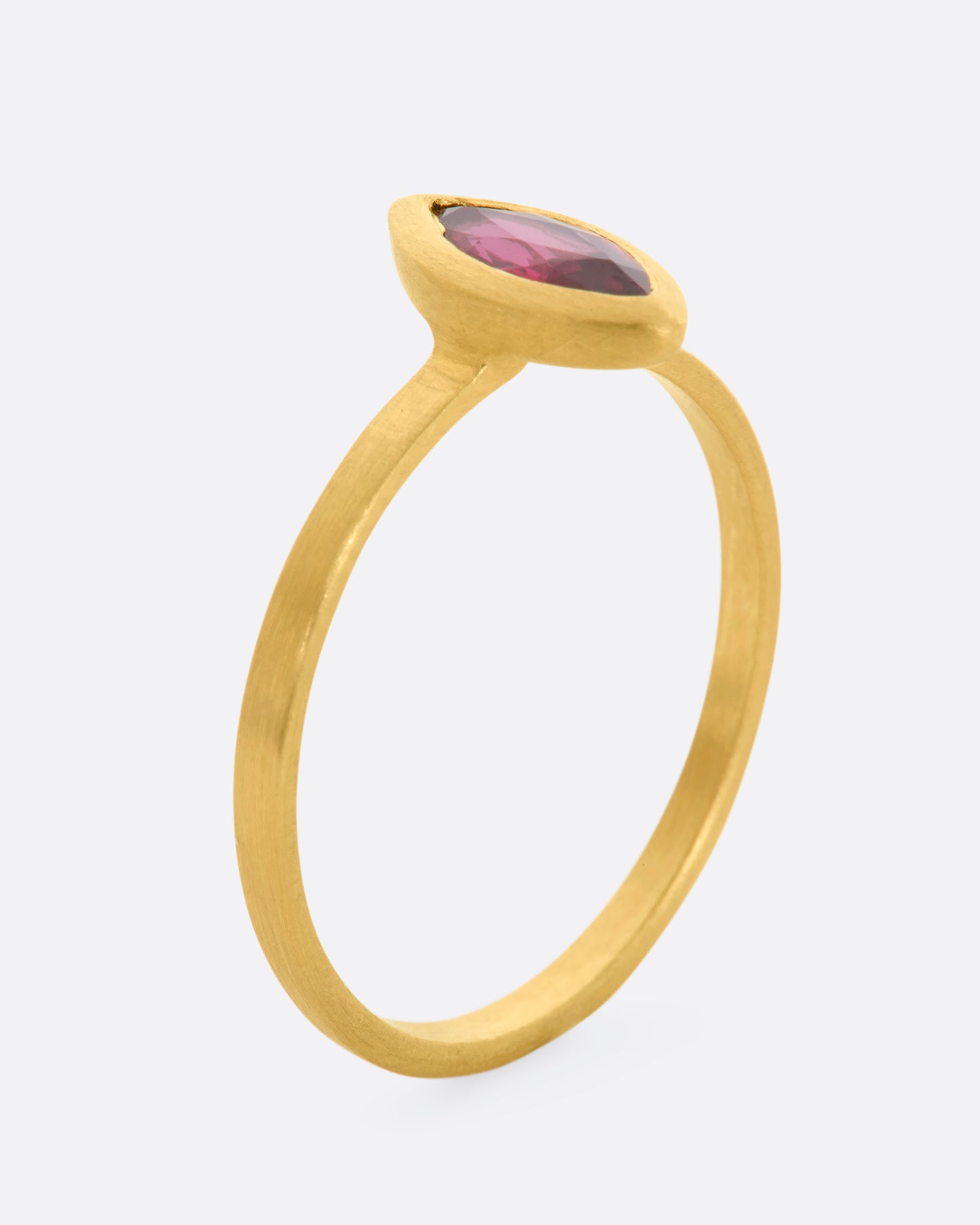 A matte yellow gold ring with a bezel set ruby marquise. View from the side standing.