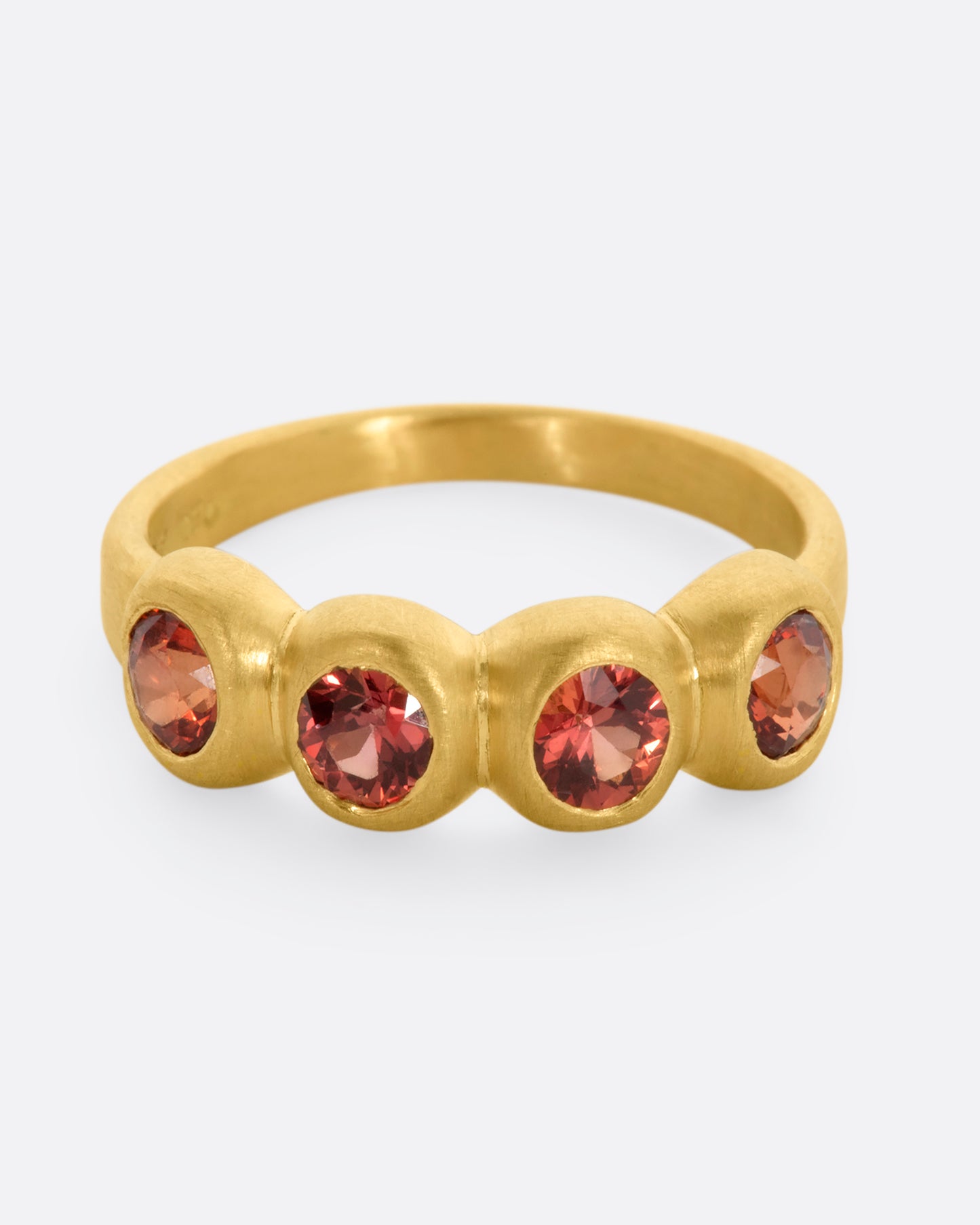 A yellow gold band with a row of four orange sapphires. Shown from the front, slightly above.