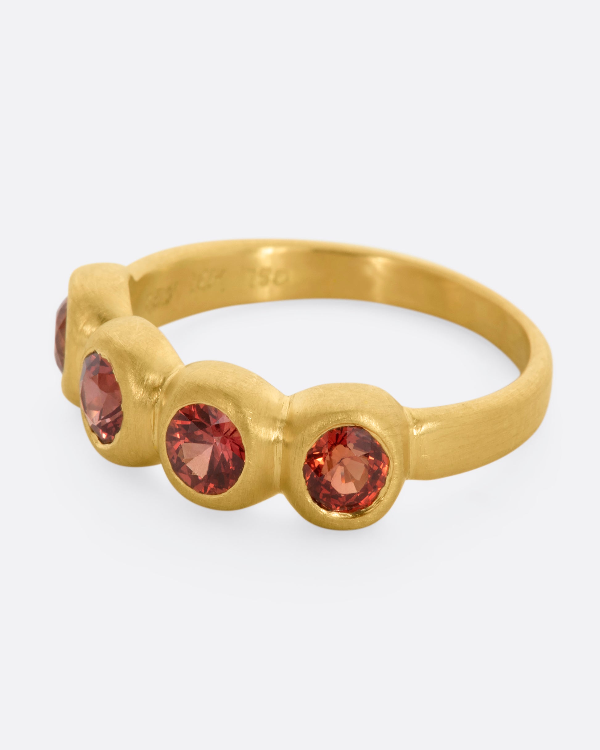 A yellow gold band with a row of four orange sapphires. Shown from the side.