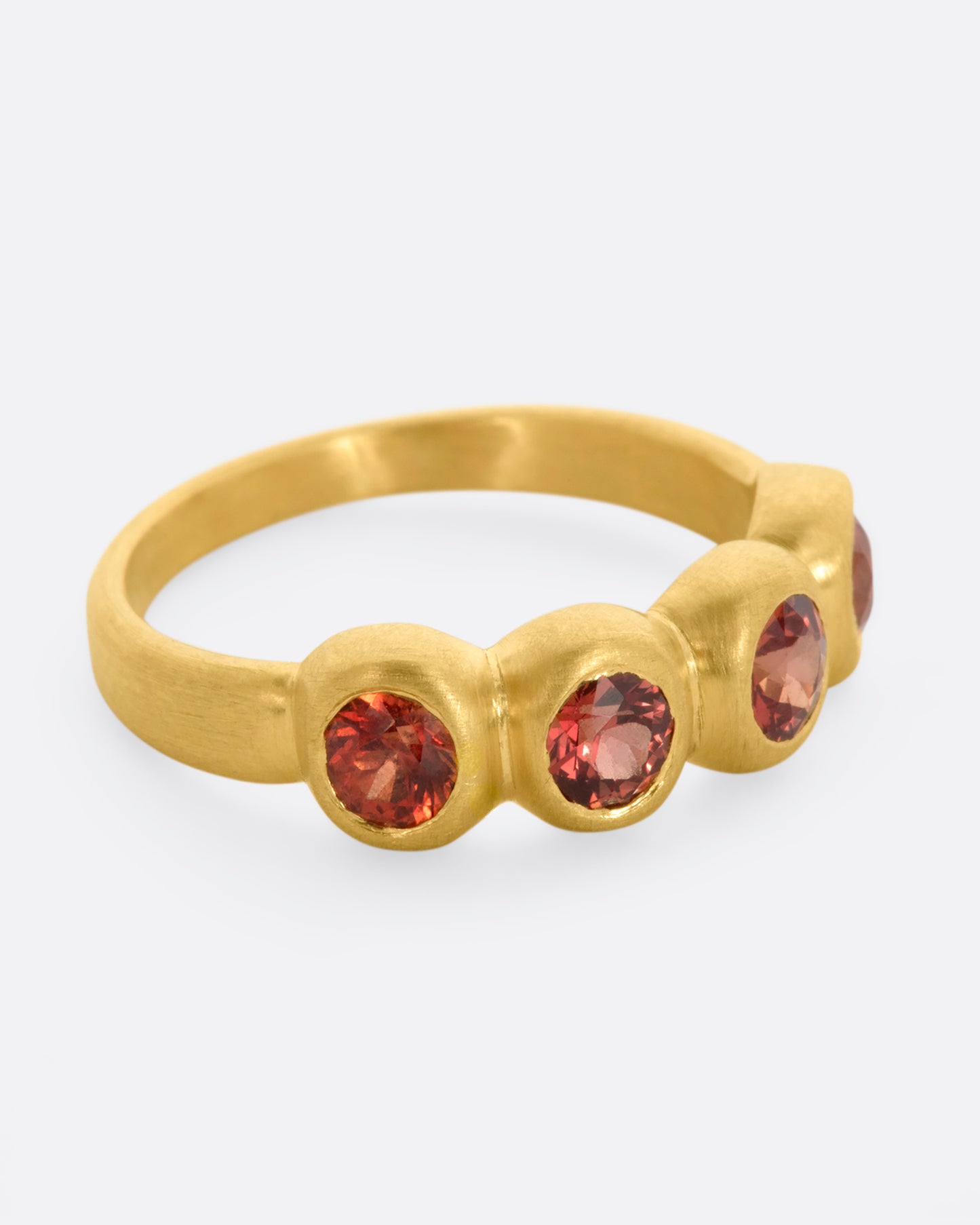 A yellow gold band with a row of four orange sapphires. Shown from the side.