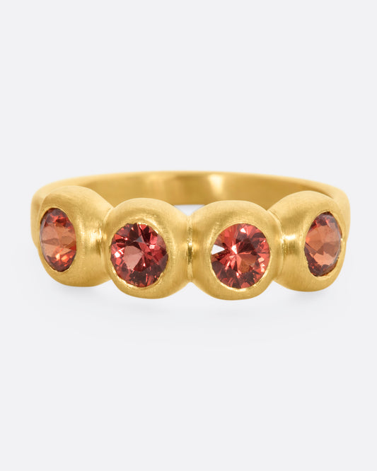 A yellow gold band with a row of four orange sapphires. Shown from the front.