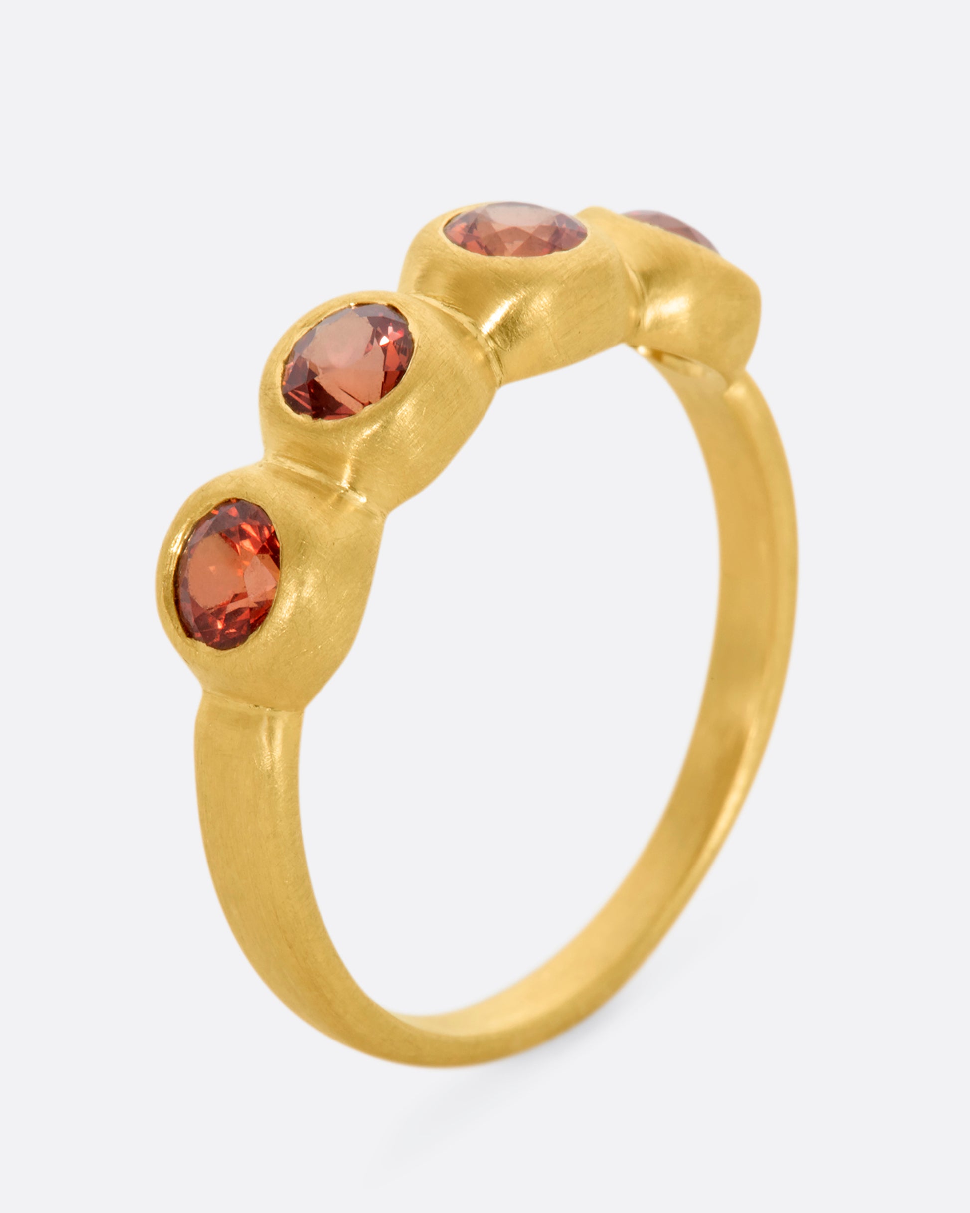 A yellow gold band with a row of four orange sapphires. Shown from the side, standing up.