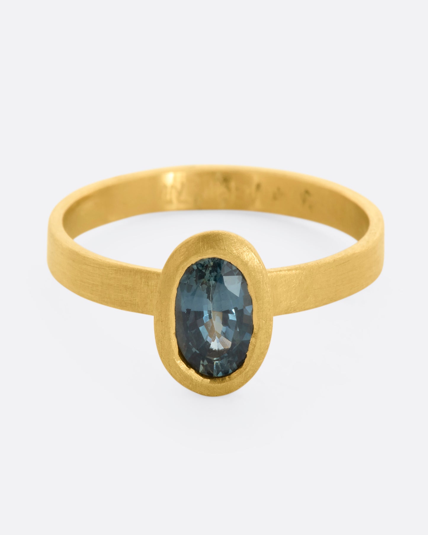 A matte yellow gold ring with an oval blue sapphire. View from the front.