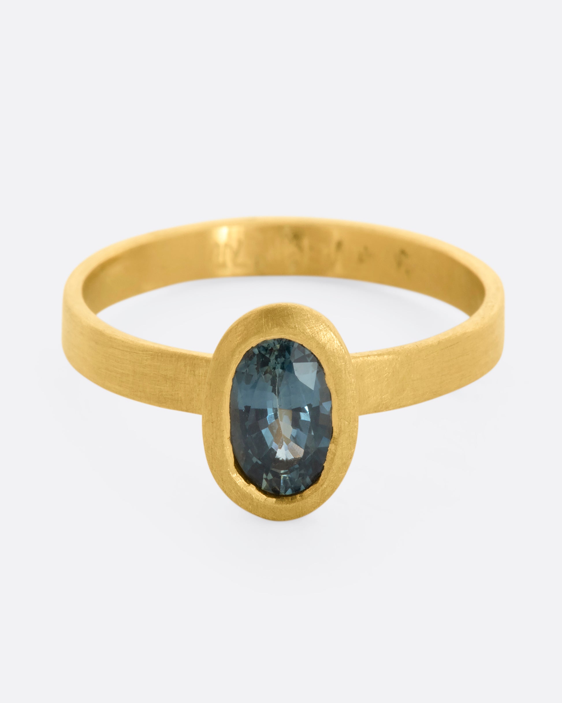 A matte yellow gold ring with an oval blue sapphire. View from the front.