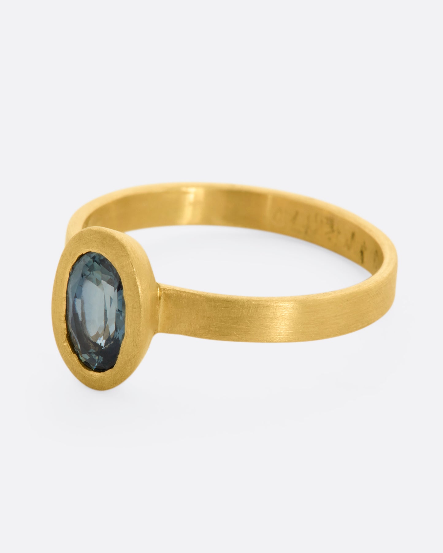 A matte yellow gold ring with an oval blue sapphire. View from the side.